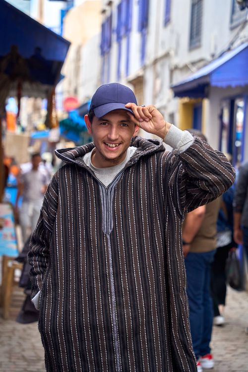 Free A smiling man in a traditional Moroccan djellaba poses on a vibrant street in Essaouira. Stock Photo