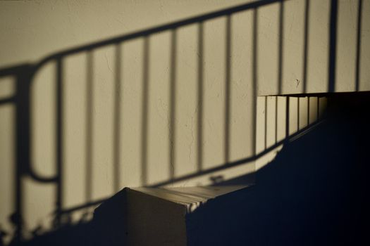 Dramatic shadows of a railing create patterns on a staircase wall.