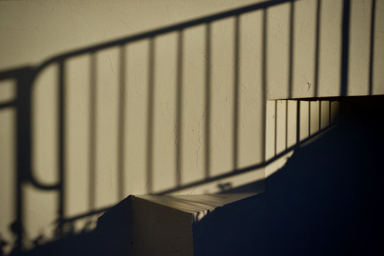 dramatic shadows of a railing create patterns on a staircase wall