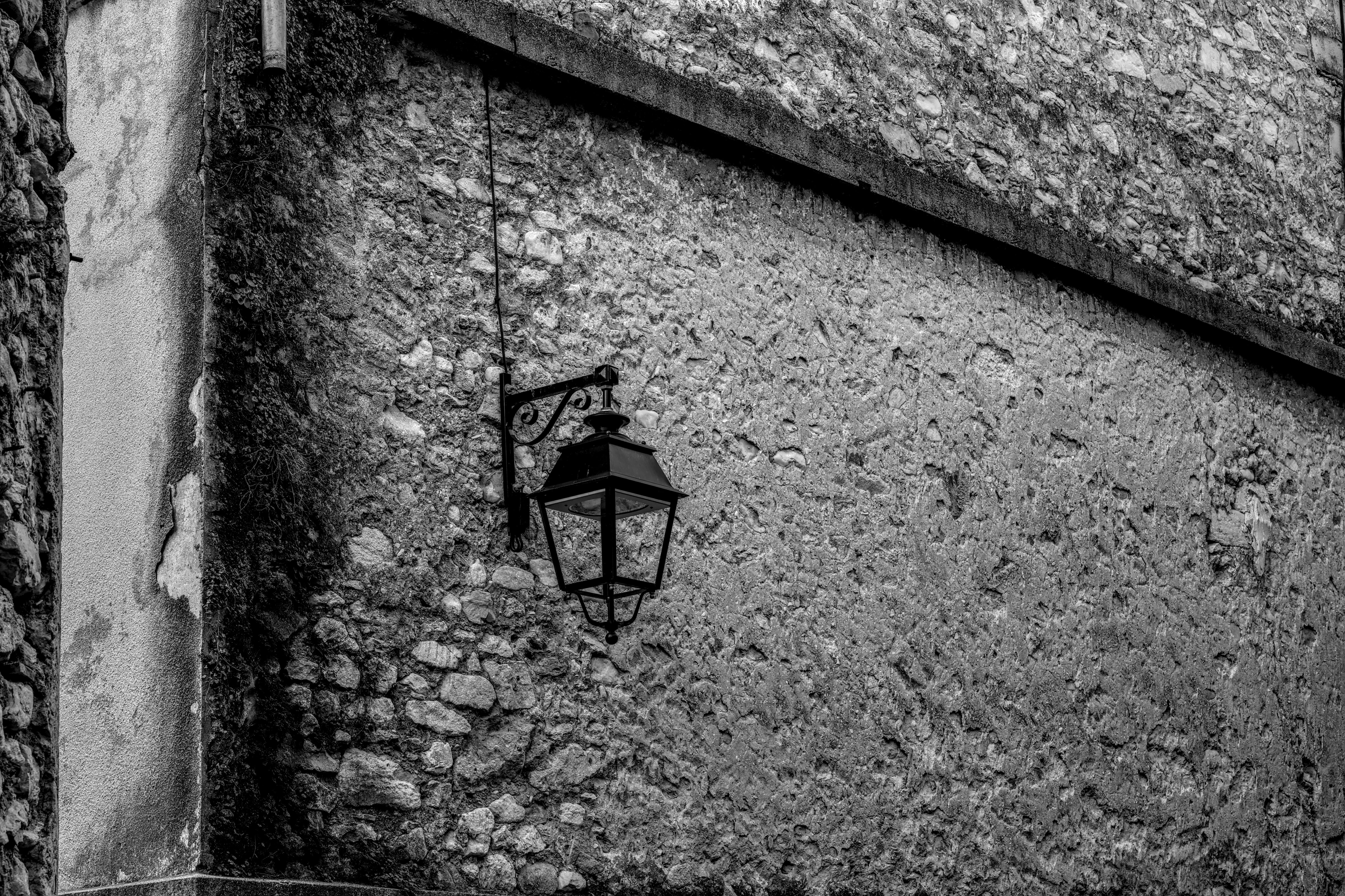 Безкоштовне Чорно-біле фото старовинного ліхтаря, встановленого на текстурованій кам'яній стіні, що передає сільський шарм. стокове фото