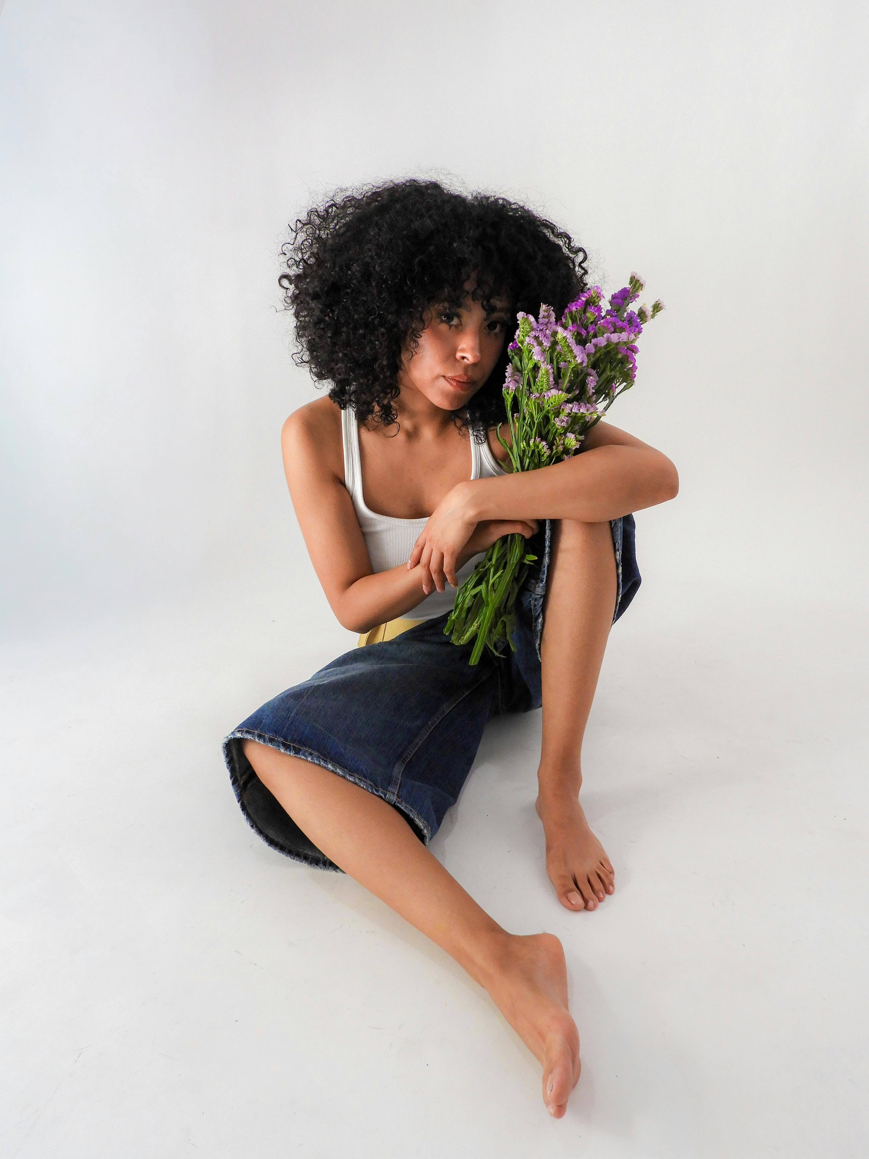 ฟรี หญิงสาวในชุดลำลองนั่งถือช่อดอกไม้ ดูงดงามและสง่างามอย่างเป็นธรรมชาติ คลังภาพถ่าย