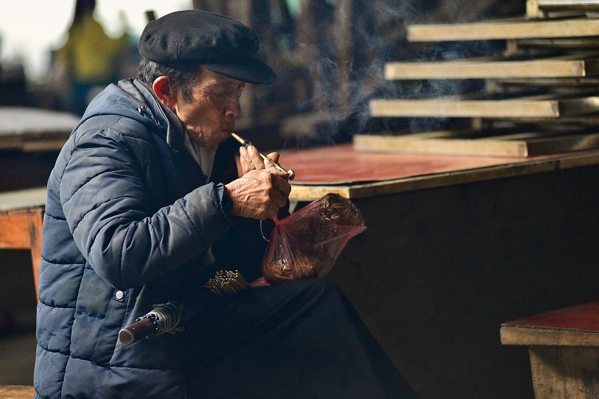 ฟรี ชายชราสวมเสื้อโค้ทหนา กำลังสูบไปป์อยู่ภายในบ้าน บรรยากาศในเมือง คลังภาพถ่าย