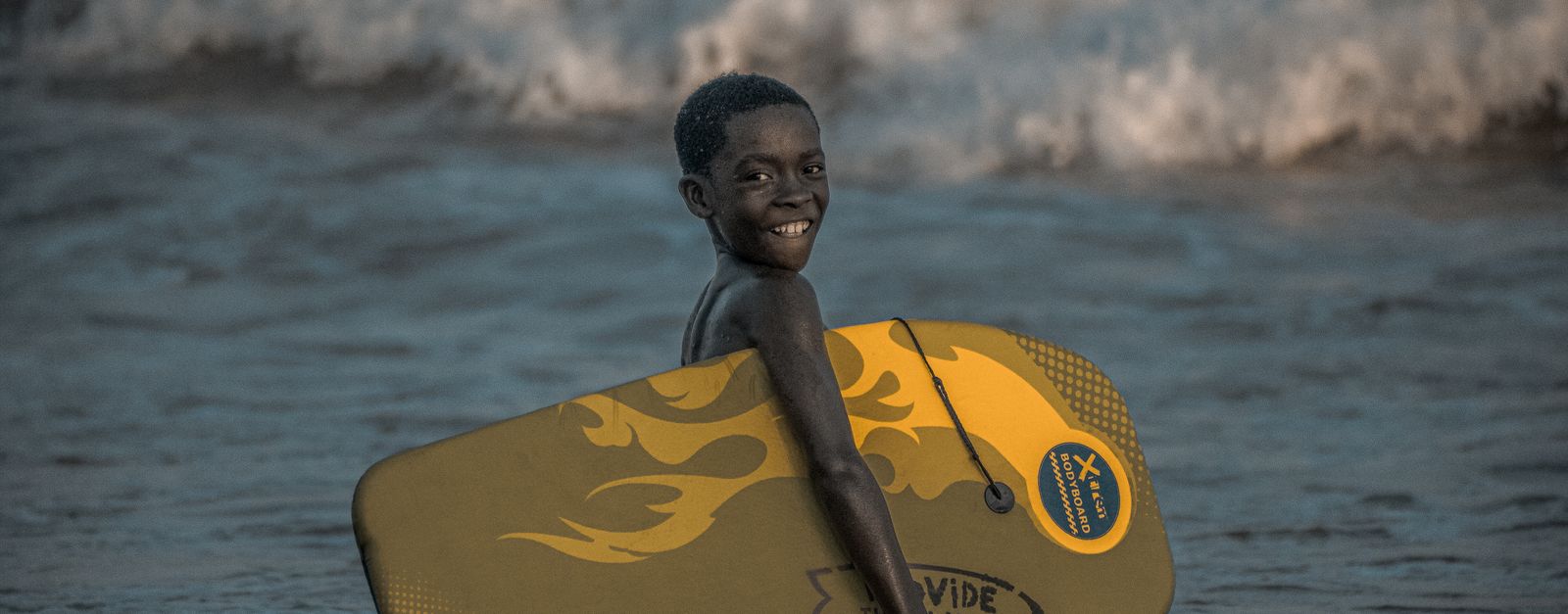 A cheerful child surfing at the beach in Takoradi, Ghana, showcasing vibrant summer fun.