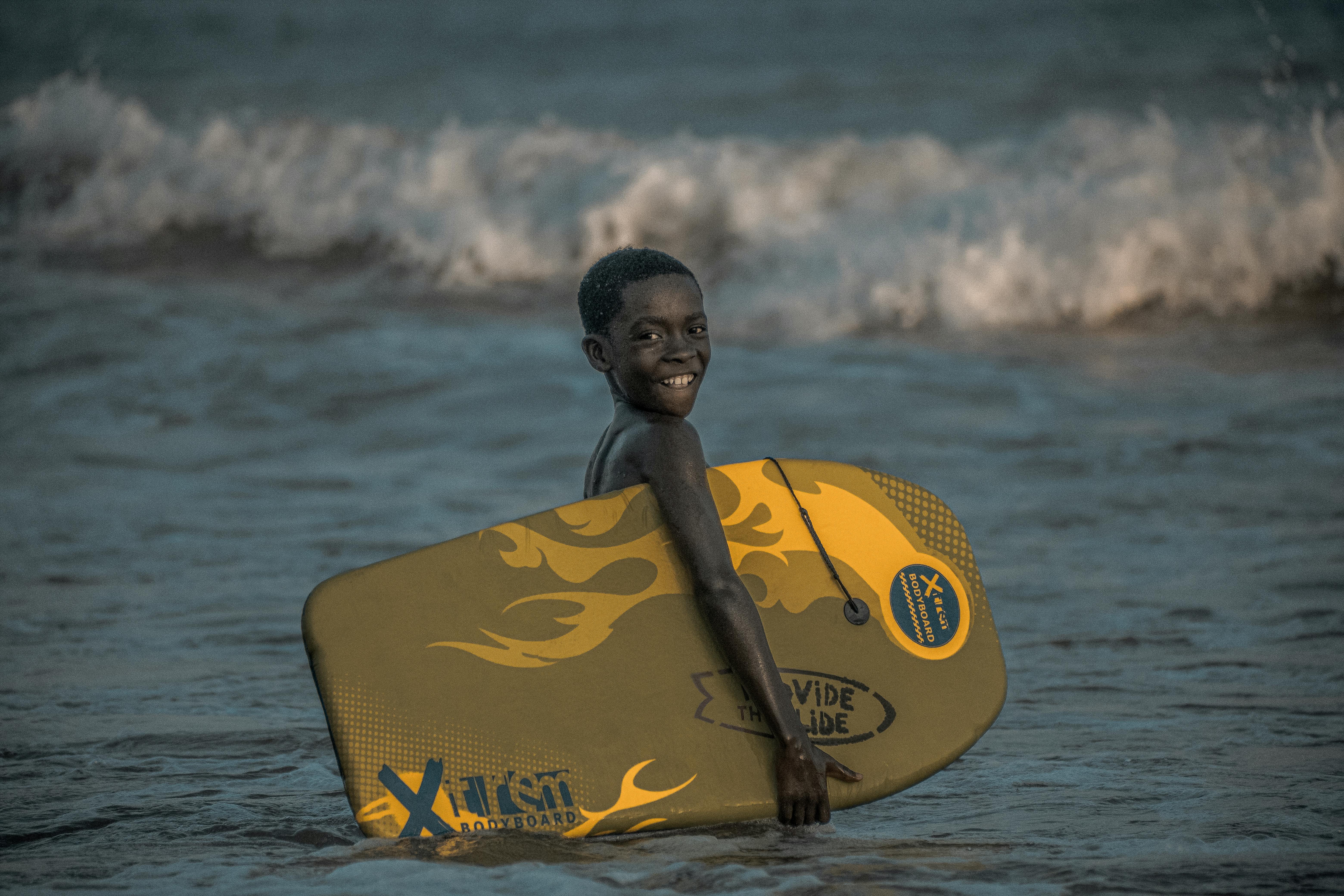 bezplatná Veselé dítě surfující na pláži v Takoradi v Ghaně předvádí pulzující letní zábavu. Základová fotografie