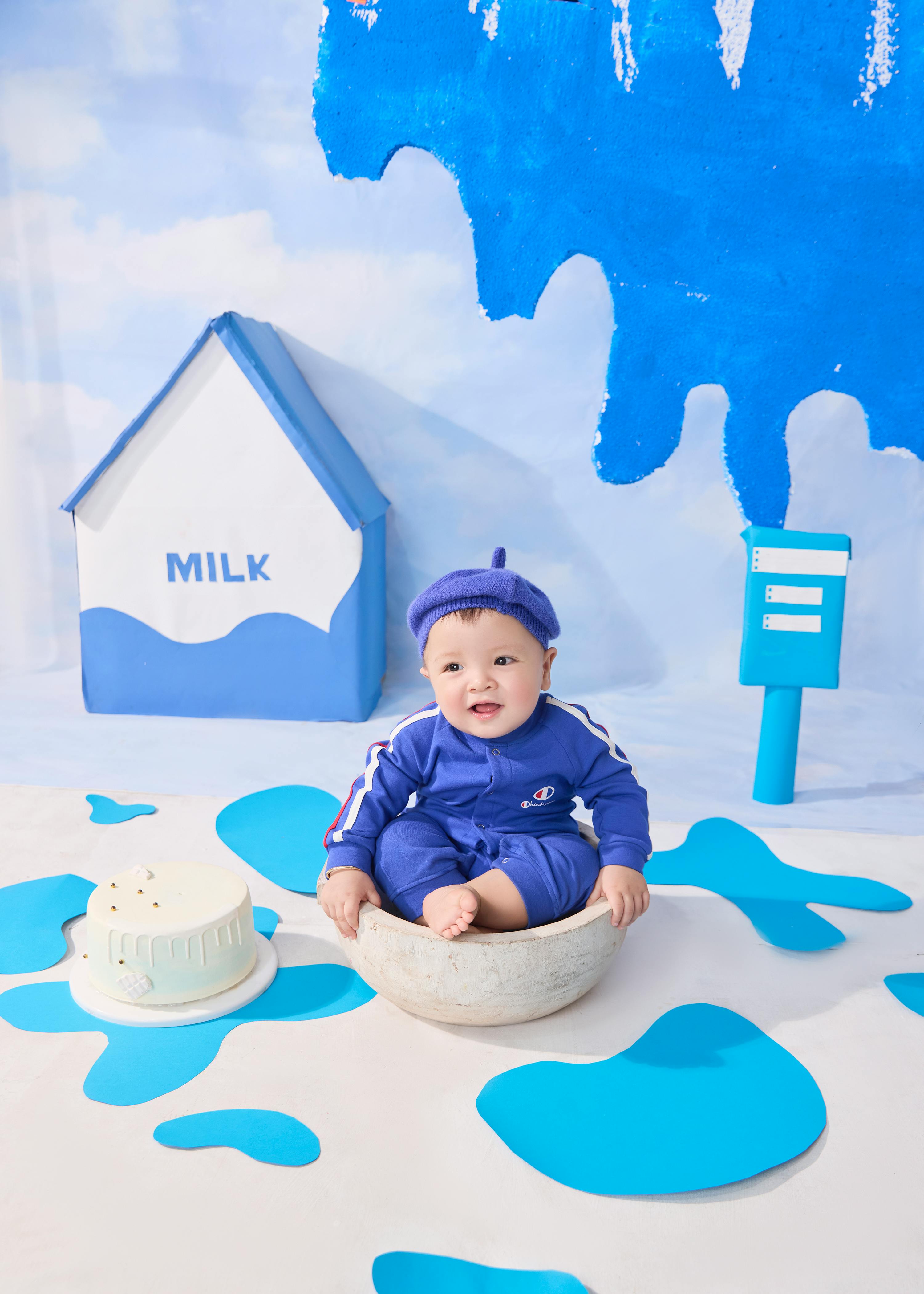 Kostnadsfria Söt bebis i blå outfit sitter i en skål med mjölktema i bakgrunden och lekfull inredning. Stock foto