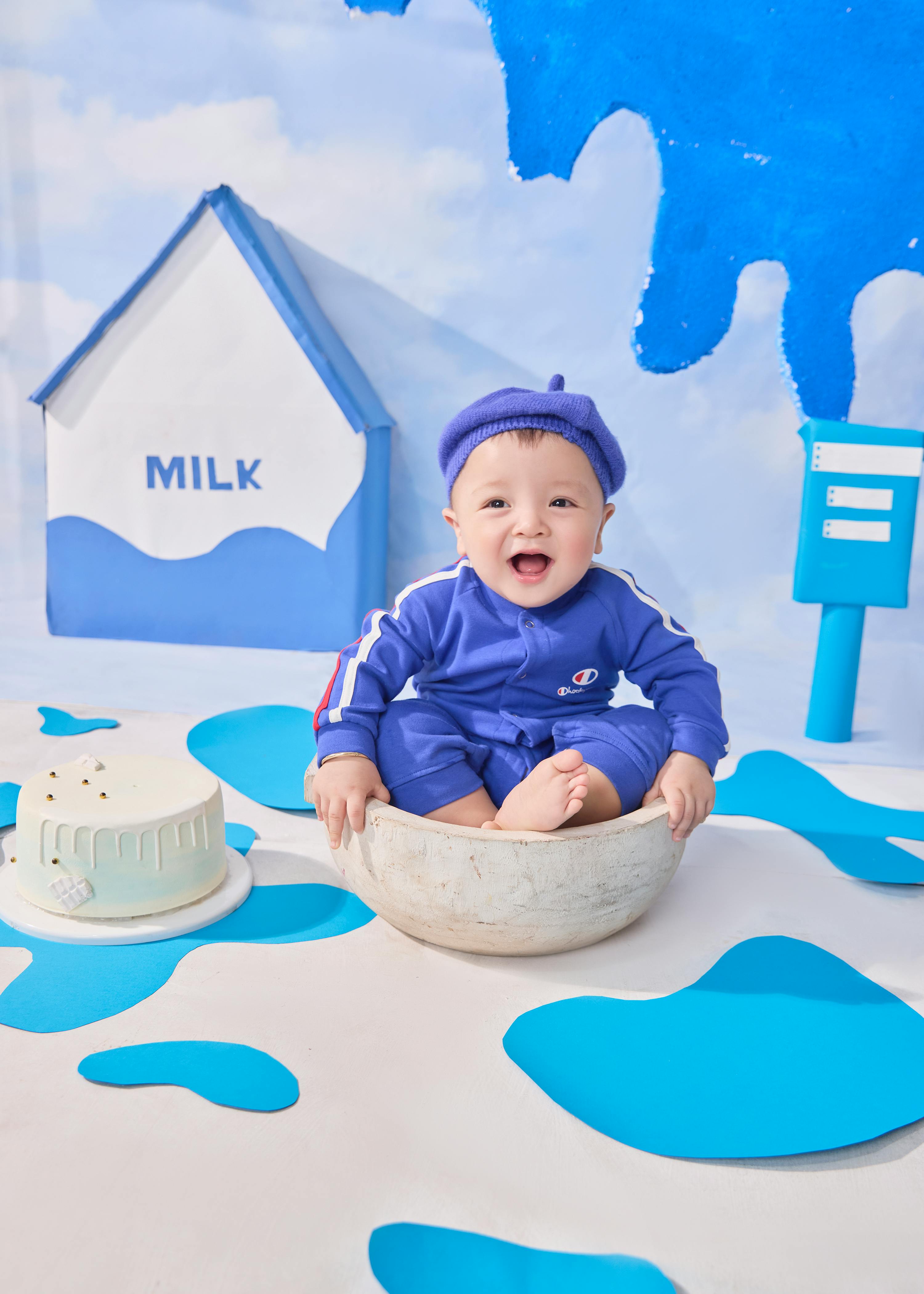 Kostnadsfria Söt bebis i en blå outfit med mjölkbakgrund och konstnärlig dekor, utstrålar glädje. Stock foto