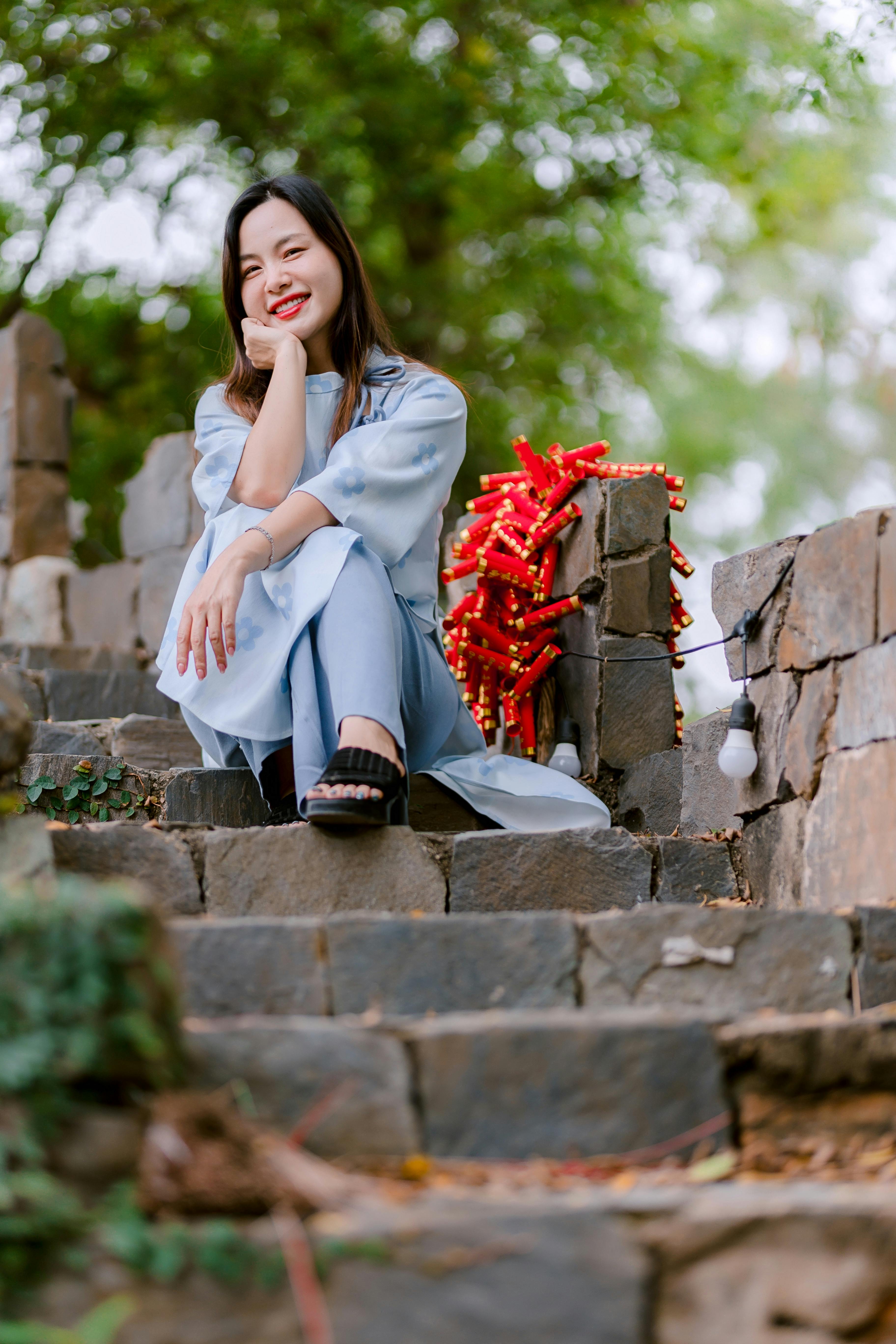 bezplatná Usmívající se žena v modrých šatech sedí na schodech venku, obklopená přírodou. Základová fotografie