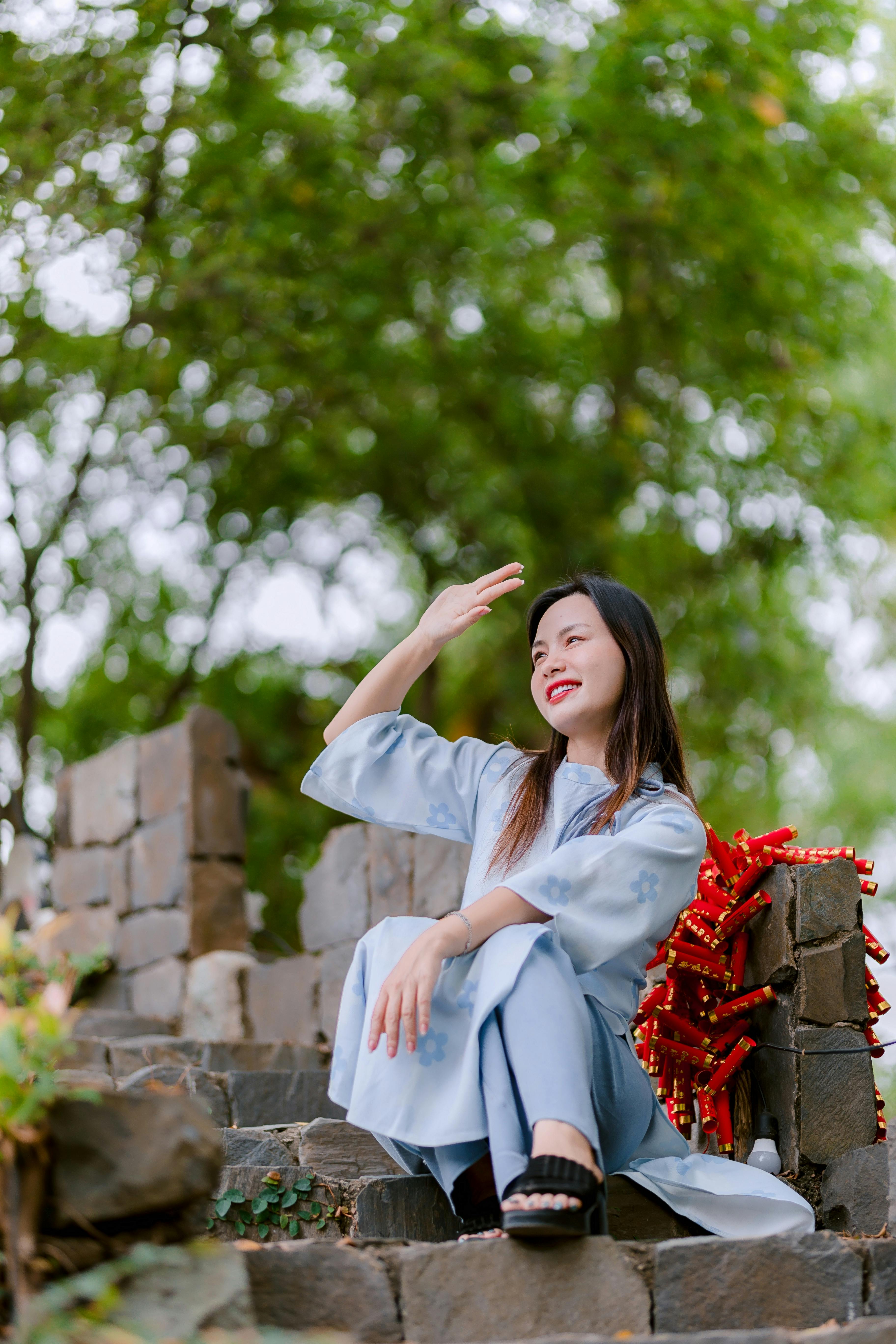 Miễn phí Một cô gái trẻ mặc váy xanh ngồi trên bậc đá bao quanh bởi cây xanh, tận hưởng khoảnh khắc yên bình ngoài trời. Ảnh lưu trữ