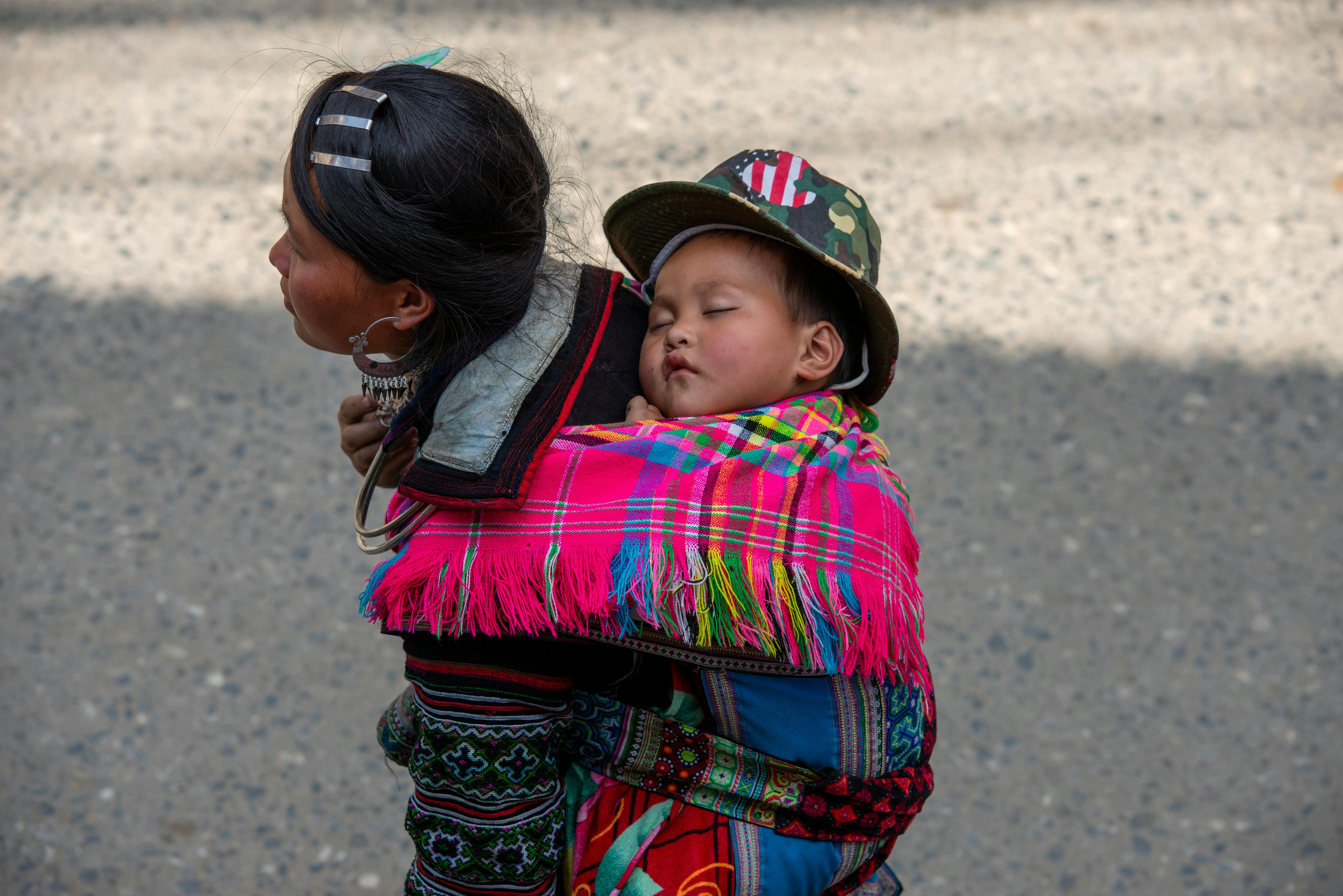 Miễn phí Một người mẹ bế con đang ngủ say trong chiếc khăn vải nhiều màu sắc vào một ngày nắng đẹp ngoài trời. Ảnh lưu trữ