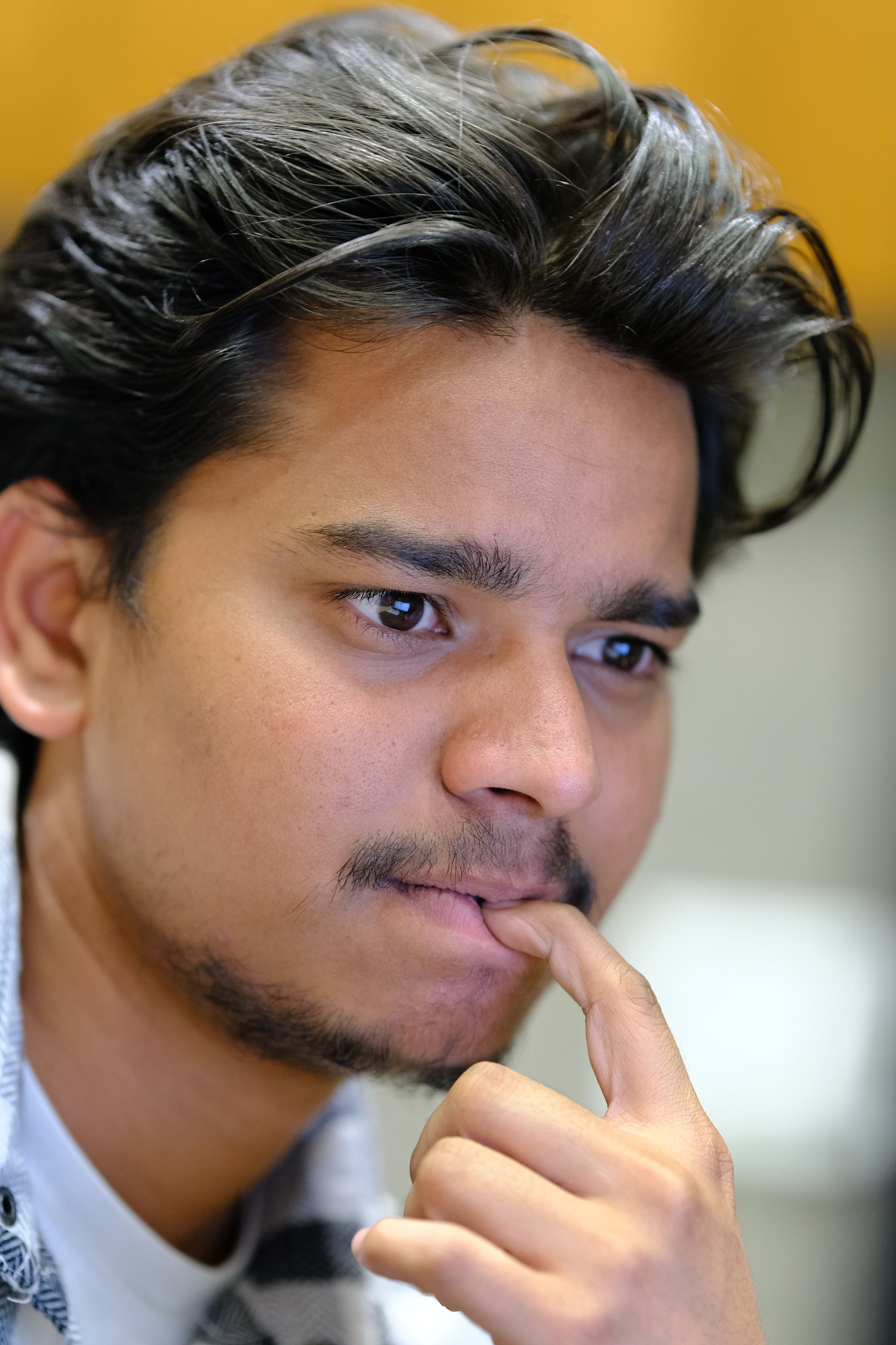 Close-up of a contemplative young man with finger on lips, looking pensive indoors.