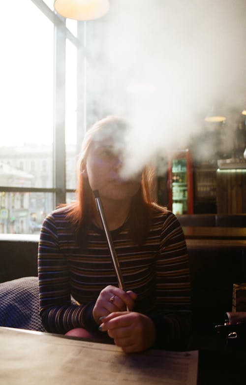 Женщина в полосатой рубашке с длинным рукавом сидит и курит