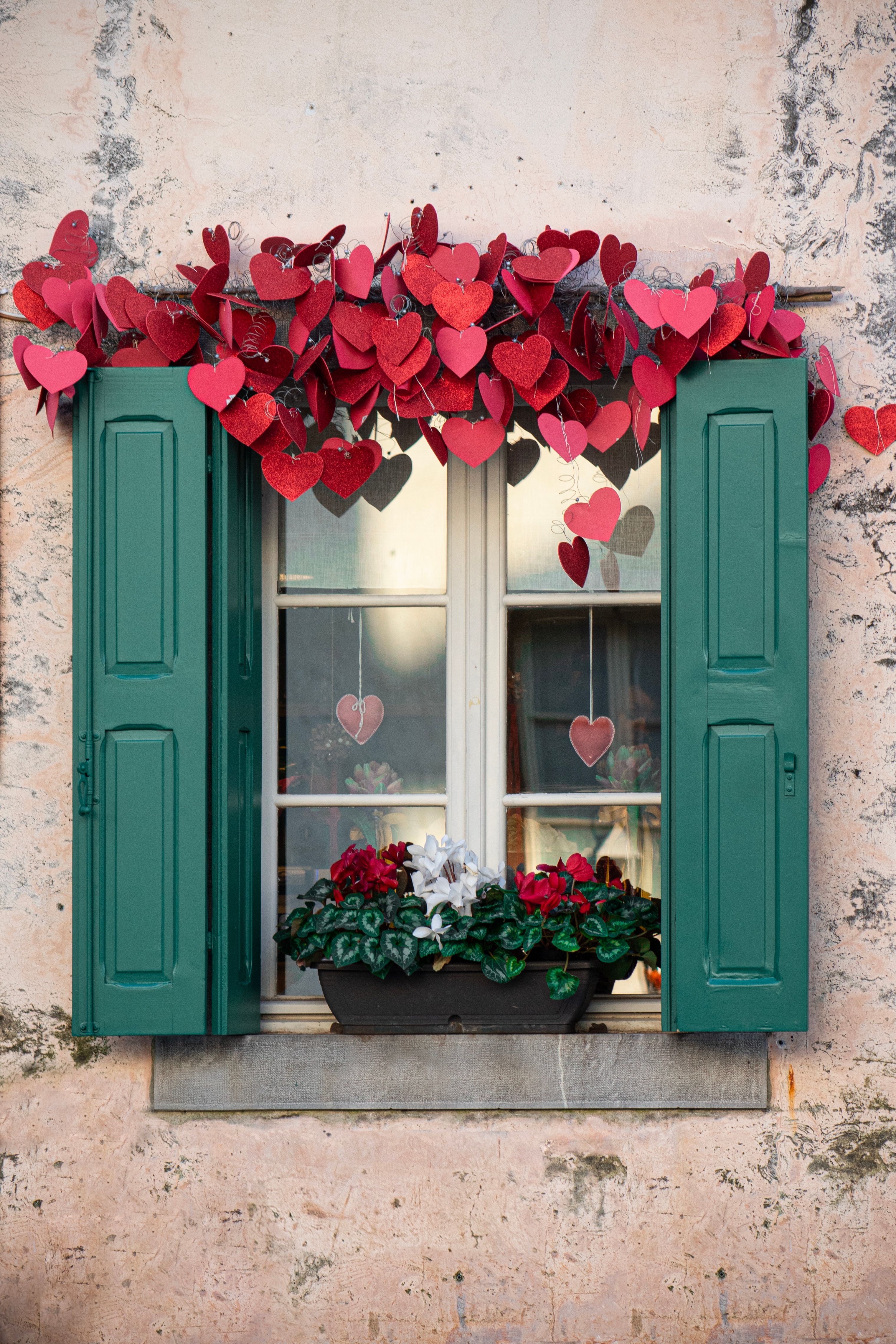 Picturesque window with heart decorations and plants in Venzone, Italy.