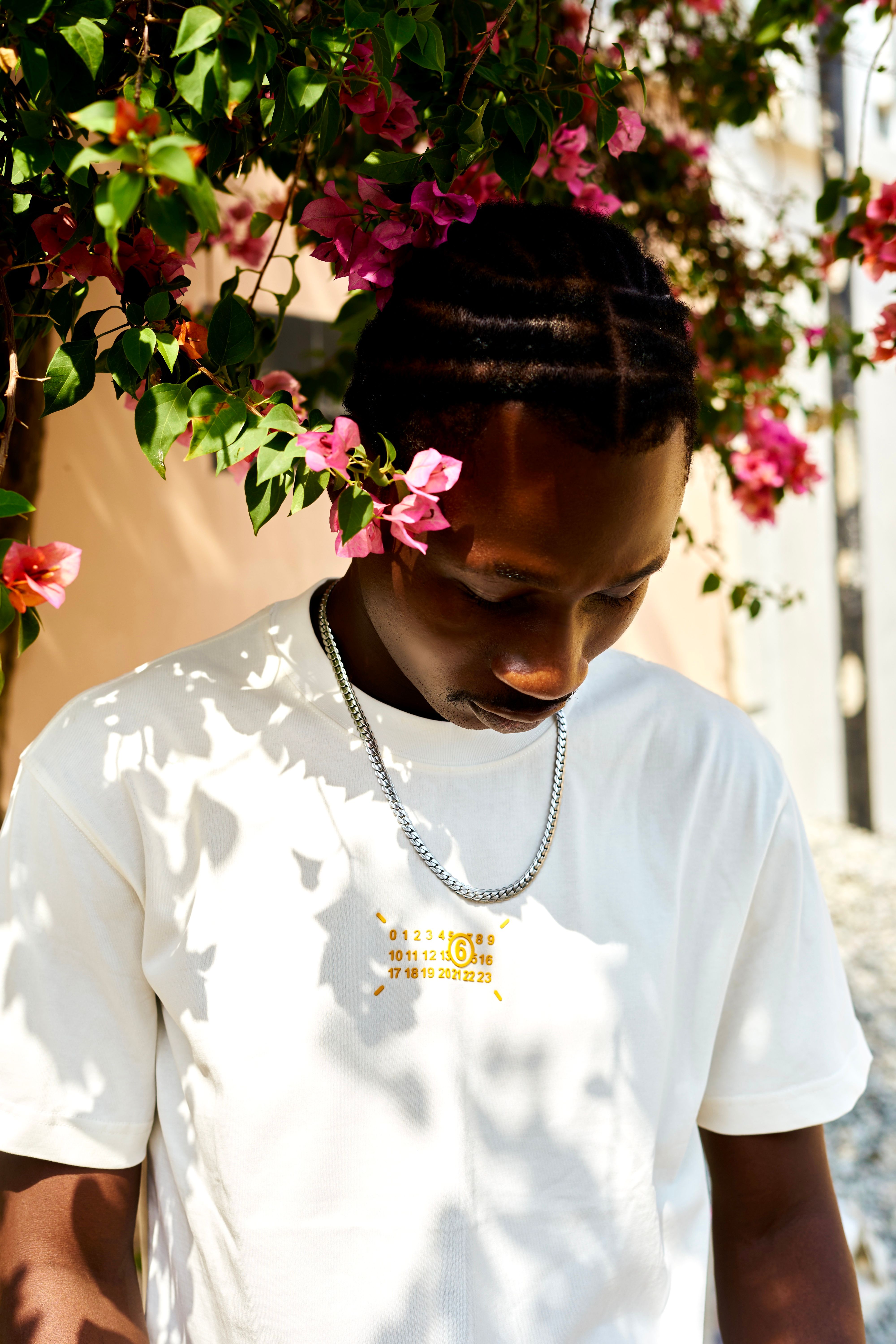 Young man in a white shirt under pink bougainvillea flowers, highlighting casual fashion.