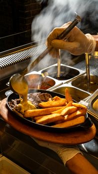 Sizzling steak with golden fries and cheese sauce in a kitchen setting.