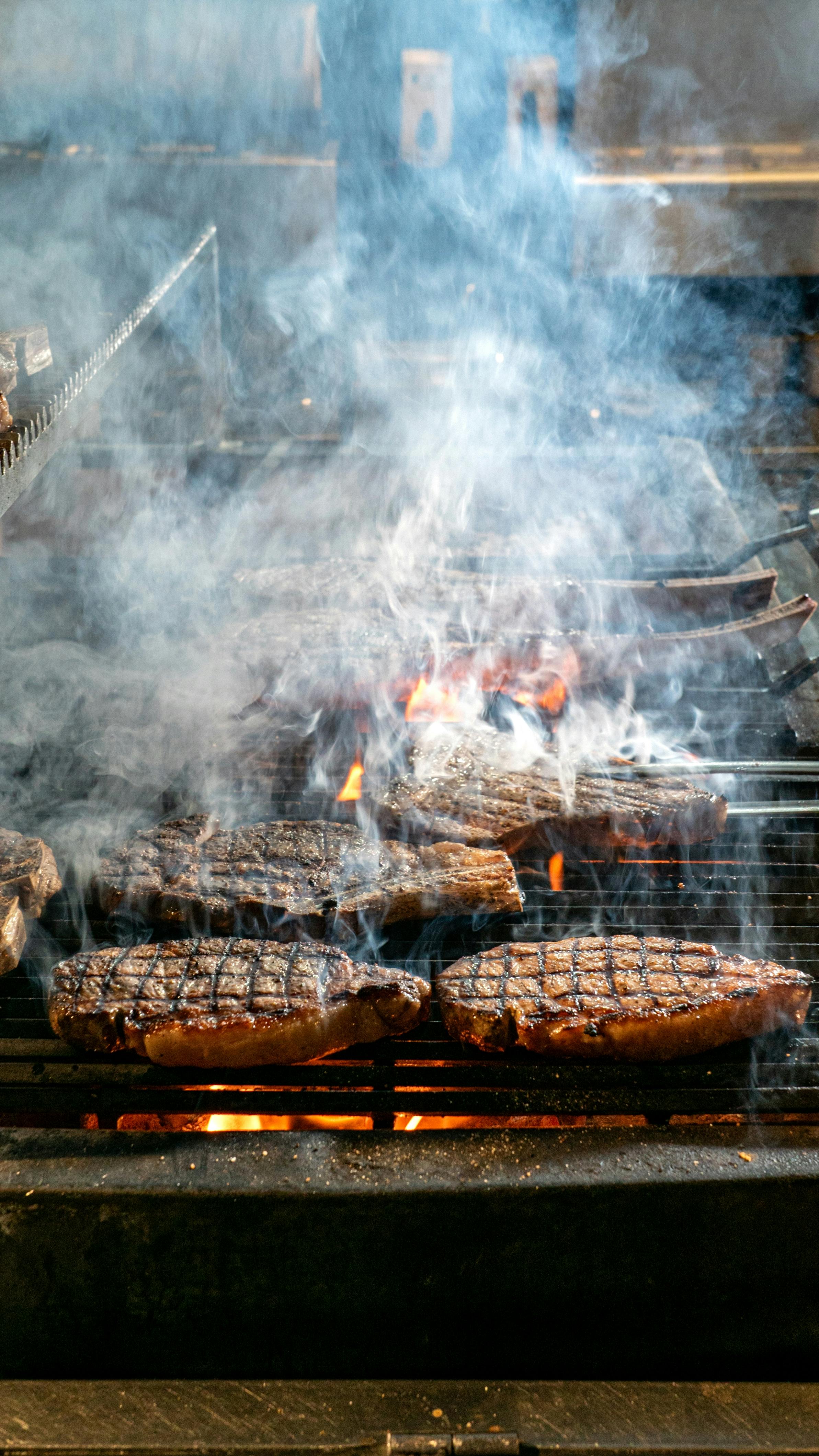 Miễn phí Cận cảnh những miếng bít tết mọng nước đang nướng với khói và lửa, ghi lại không khí nướng thịt ngoài trời. Ảnh lưu trữ