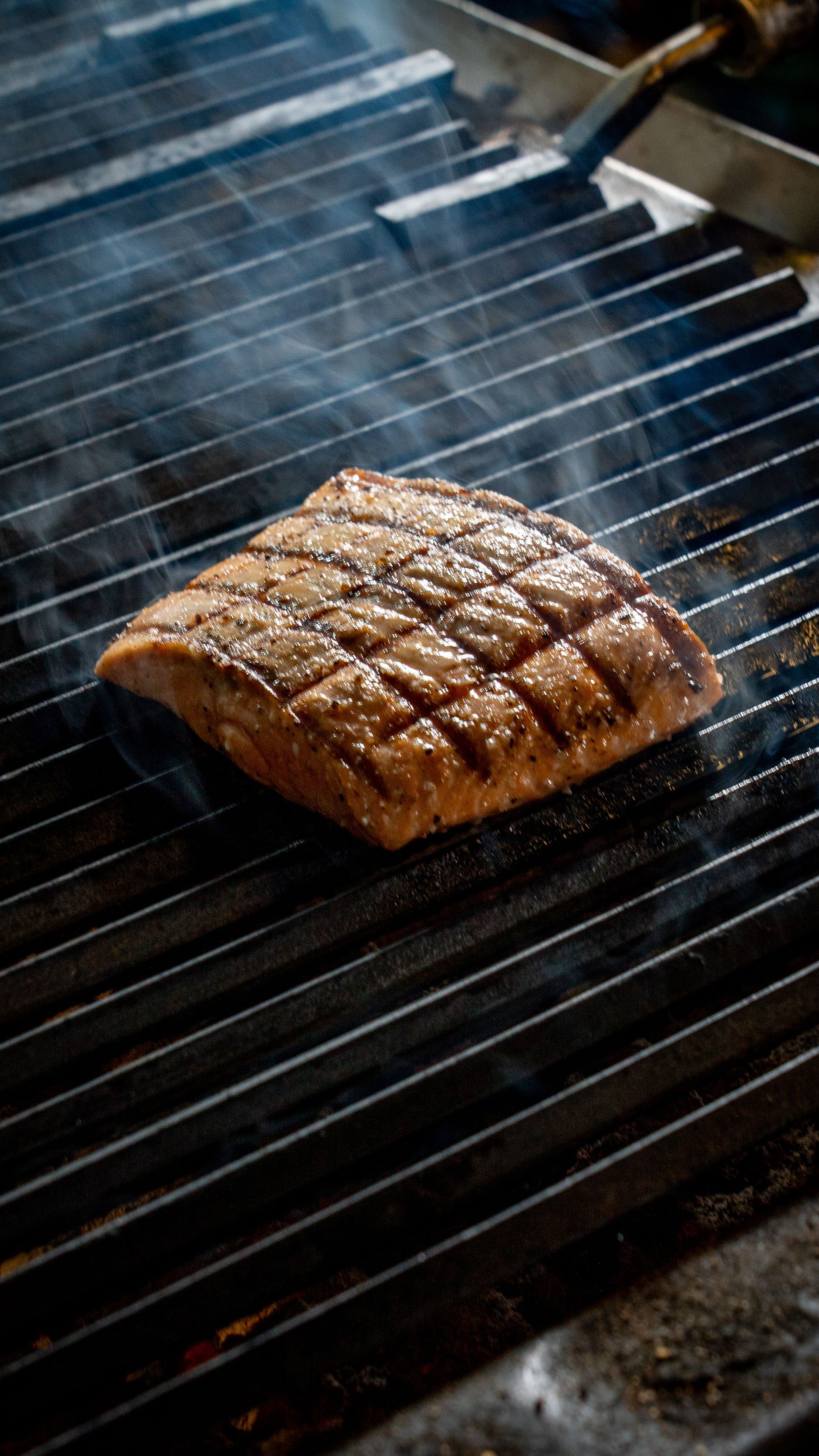 Delicious grilled salmon steak with grid marks on a grill emitting smoke for a tasty meal.