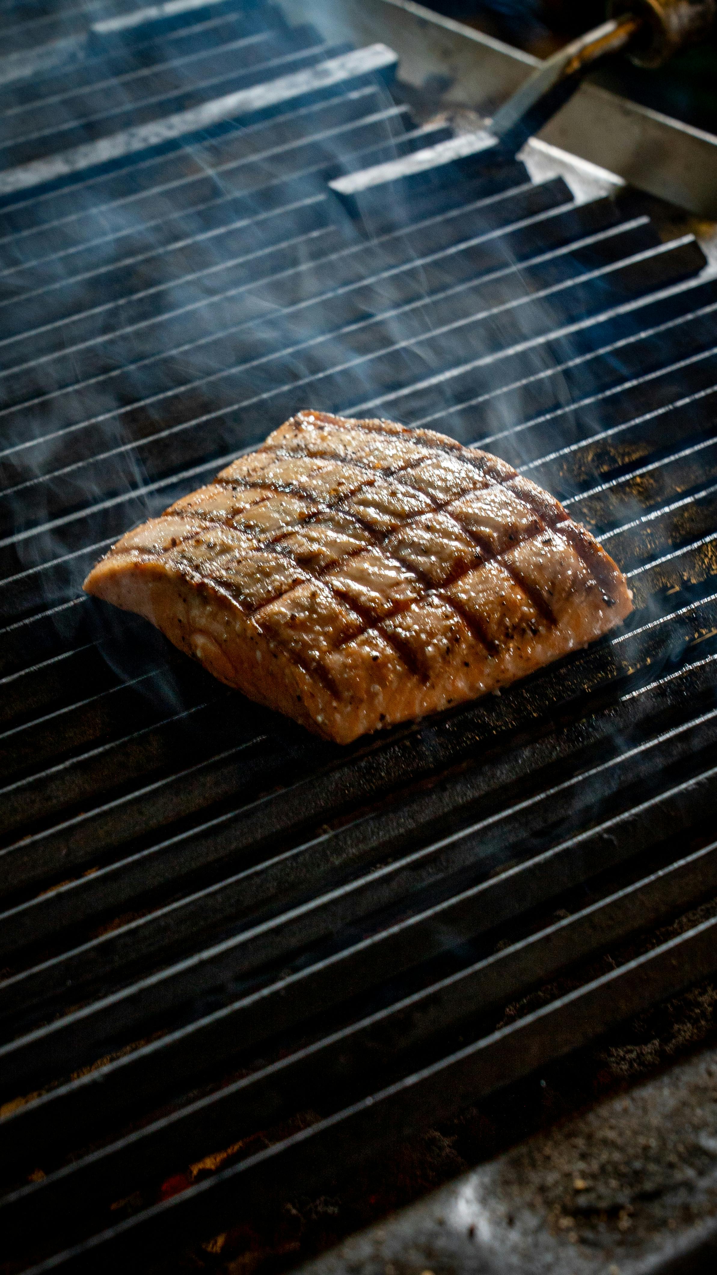Kostnadsfria Läcker grillad laxbiff med rutmönster på ett galler som avger rök för en god måltid. Stock foto