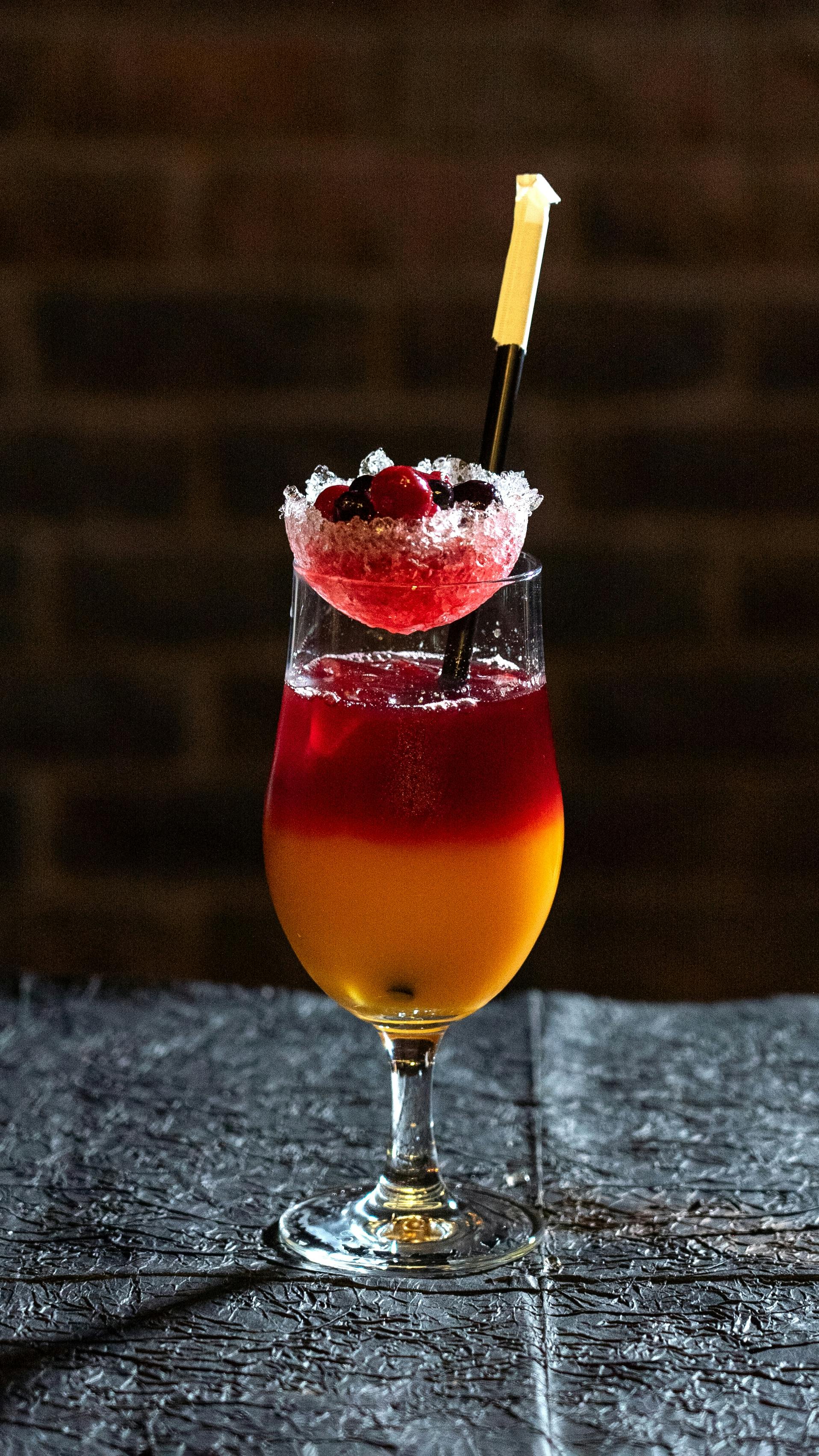 Gratuit Cocktail coloré servi dans un verre élégant, garni de fruits et baigné d'une lumière tamisée. Photos
