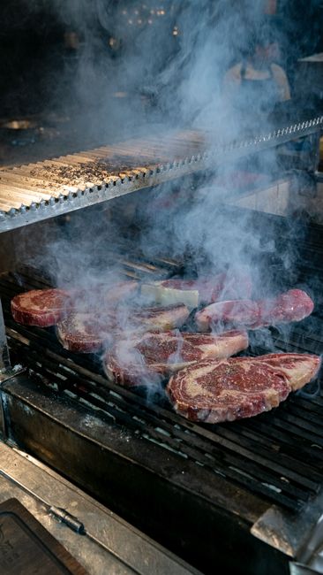 Fotomural Primer plano de jugosos bisteces sazonados chisporroteando sobre una parrilla humeante, perfecto para amantes de las barbacoas.