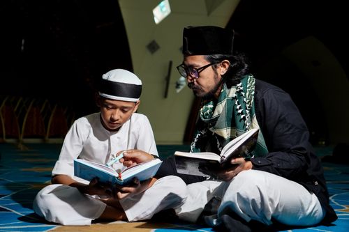 Free A father and son reading religious texts on the floor in a mosque, fostering learning and connection. Stock Photo