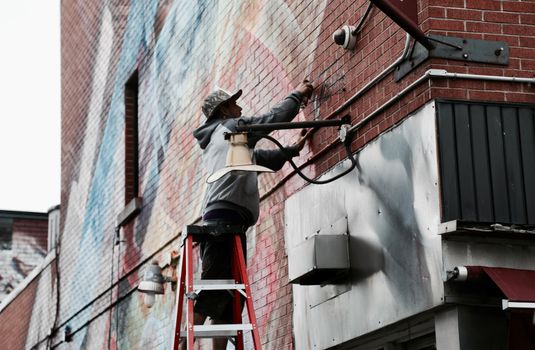 A worker on a ladder installs a security camera on a colorful graffiti-covered brick wall in Montreal.