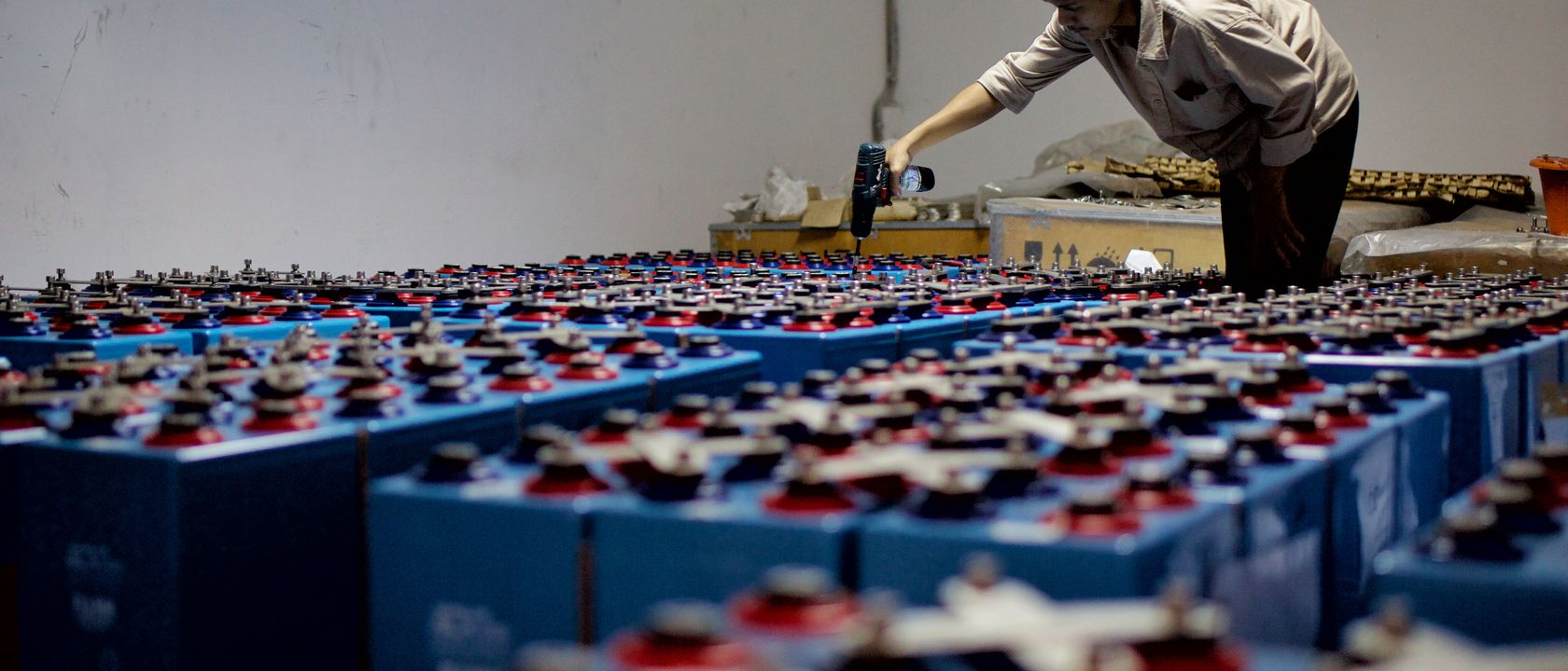 A worker checking many industrial batteries inside a facility. Indoor, industrial setting.