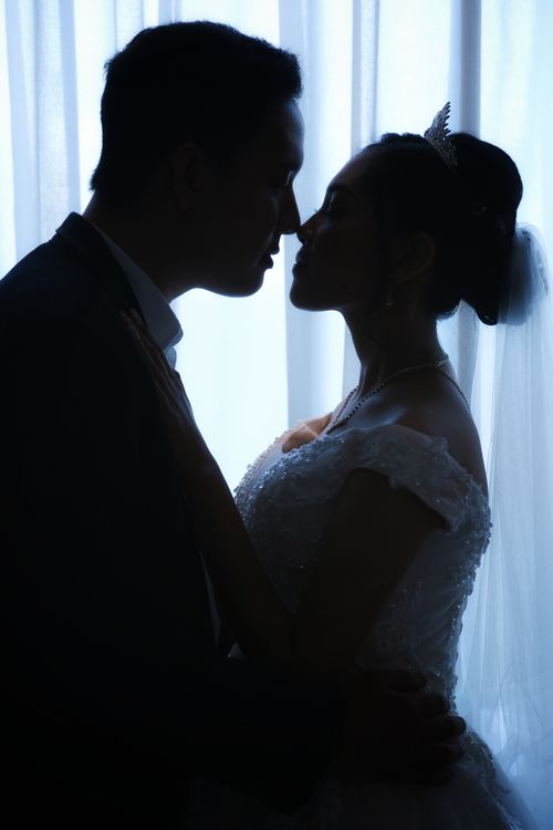 Free Romantic silhouette of a couple sharing a kiss on their wedding day, bride in elegant gown. Stock Photo