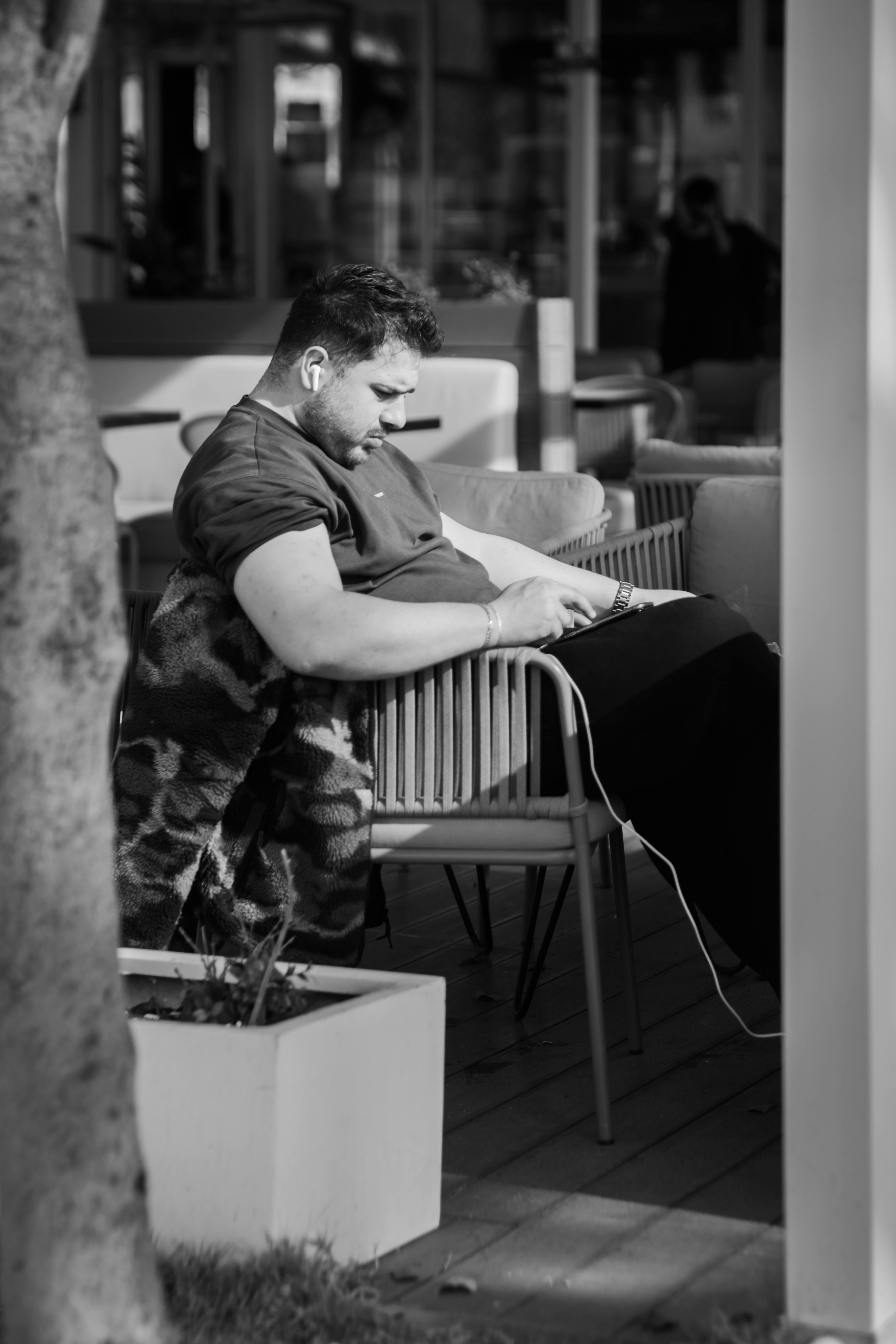 ingyenes Egy férfi töprengve ül a szabadban egy modern székben, és elmerül a telefonjában. Stockfotó