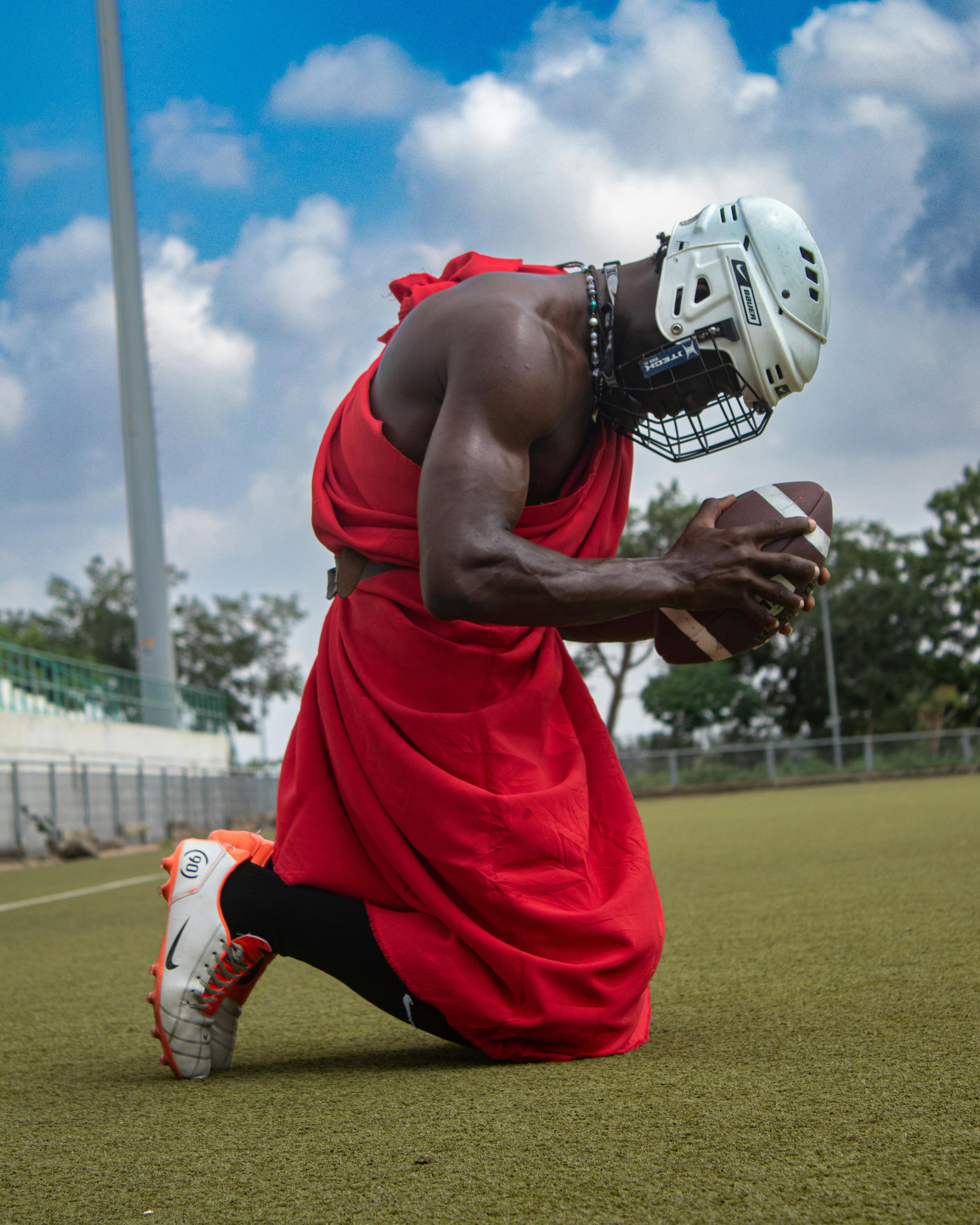 A man in traditional attire plays American football, blending culture with sport under a vibrant sky.
