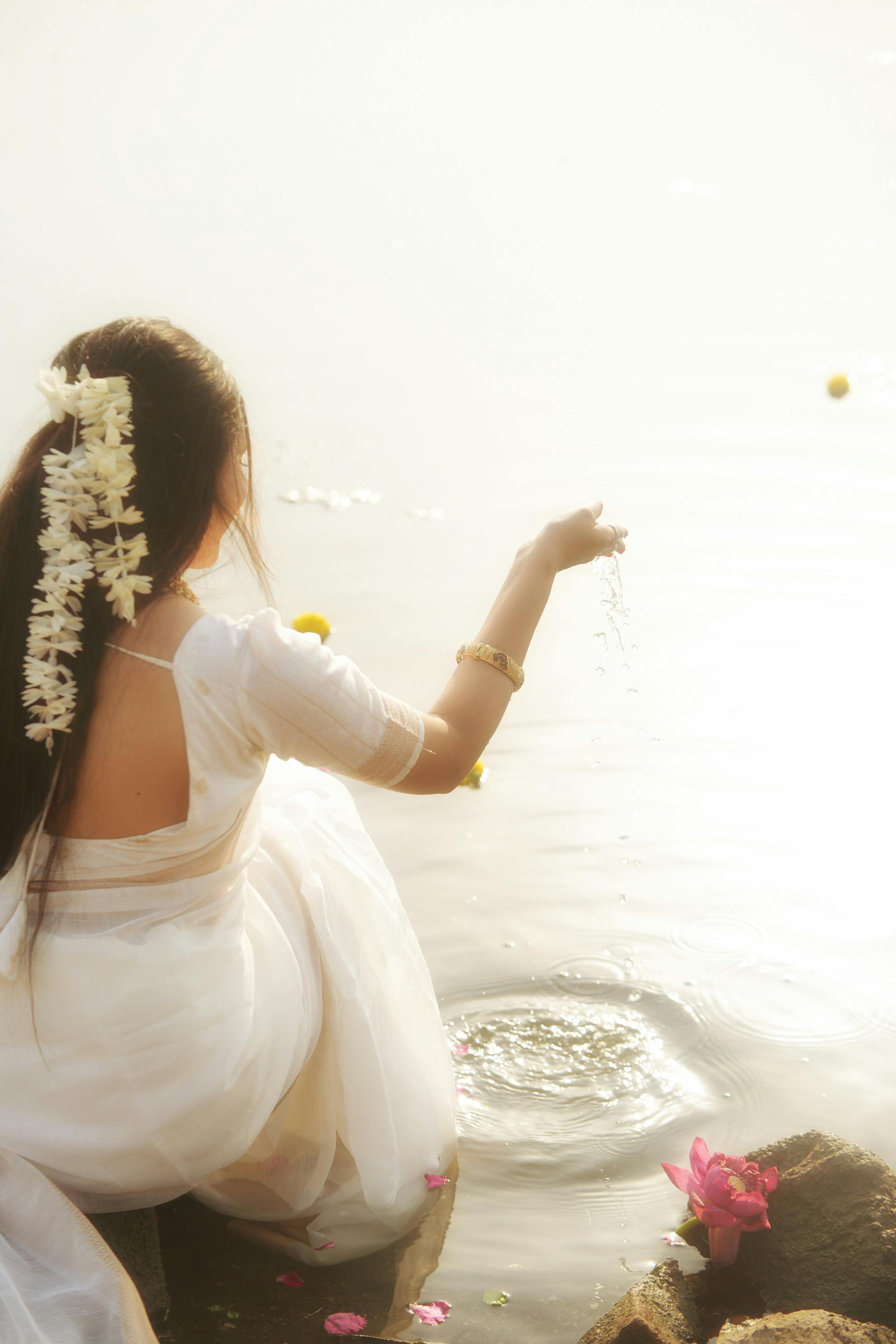 免費 一位身穿白色傳統服飾的女子在寧靜的湖邊舉行儀式，周圍鮮花環繞。 圖庫相片