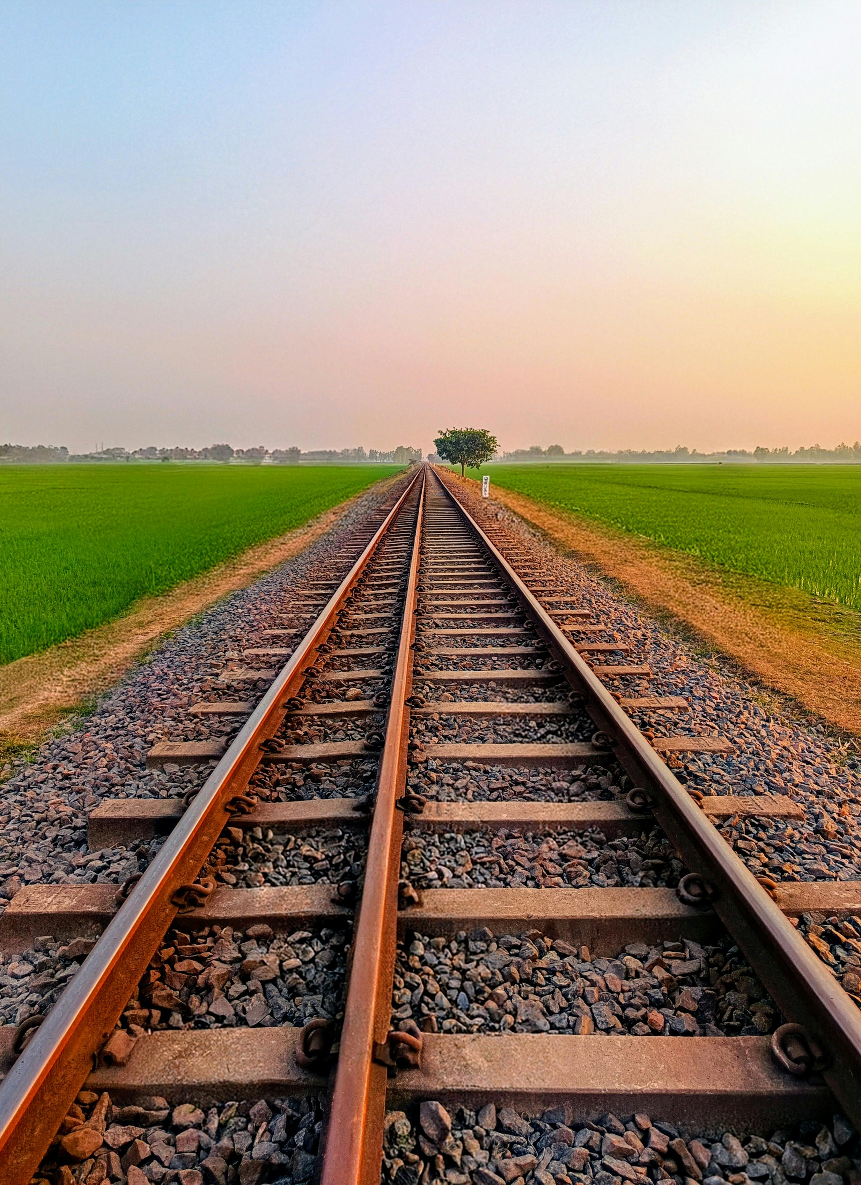 무료 고요한 석양 아래 푸른 들판을 가로지르는 철로의 아름다운 풍경. 스톡 사진