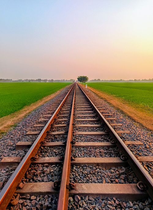 Free Stunning view of railroad tracks stretching through lush green fields under a serene sunset sky. Stock Photo