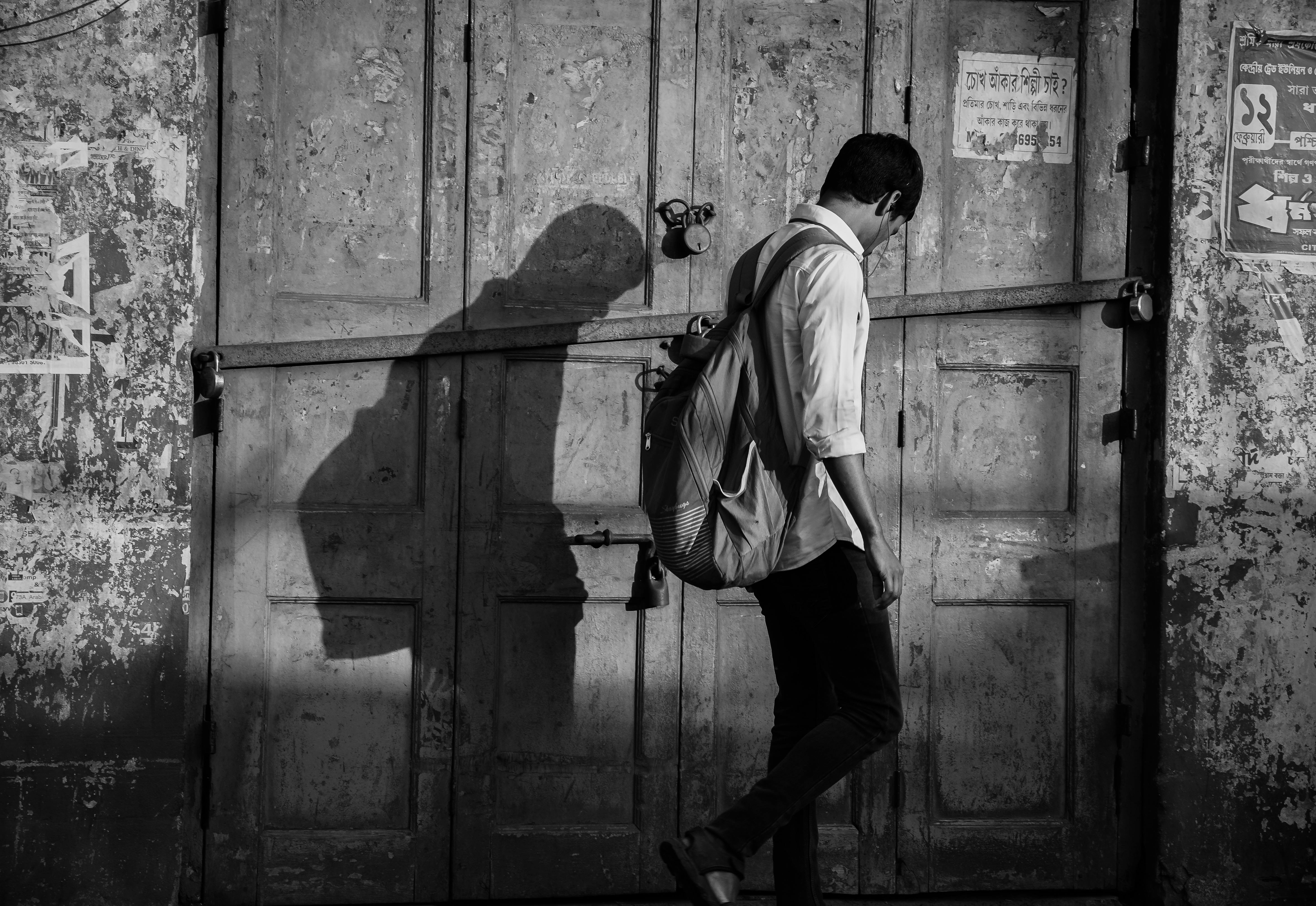 Zadarmo Čiernobiely záber muža s batohom, ktorý vrhá tieň na rustikálne dvere. Fotka z fotobanky