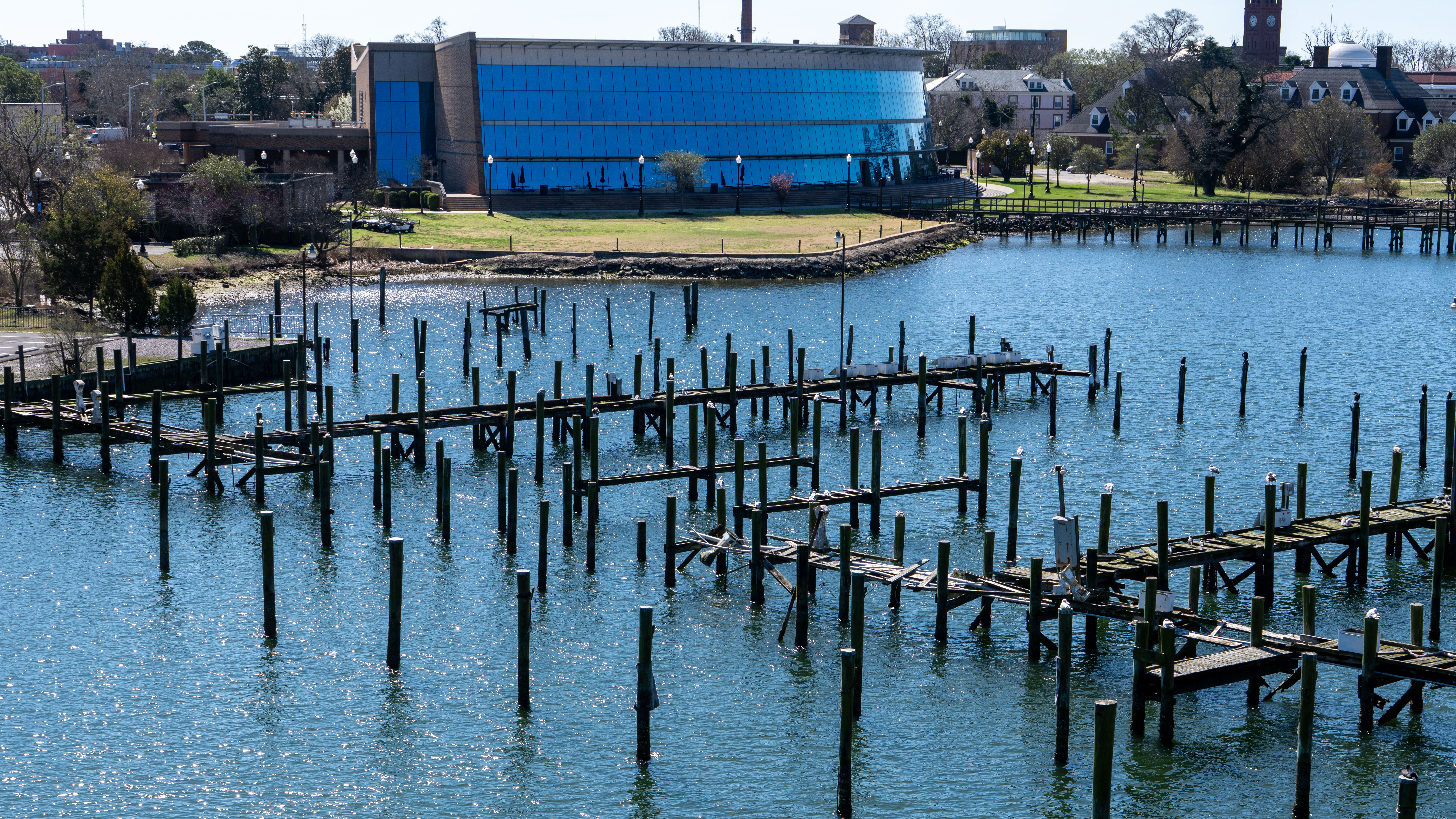 Aerial view of a waterfront and wooden pier in Hampton, Virginia with calm waters and cityscape in the background.