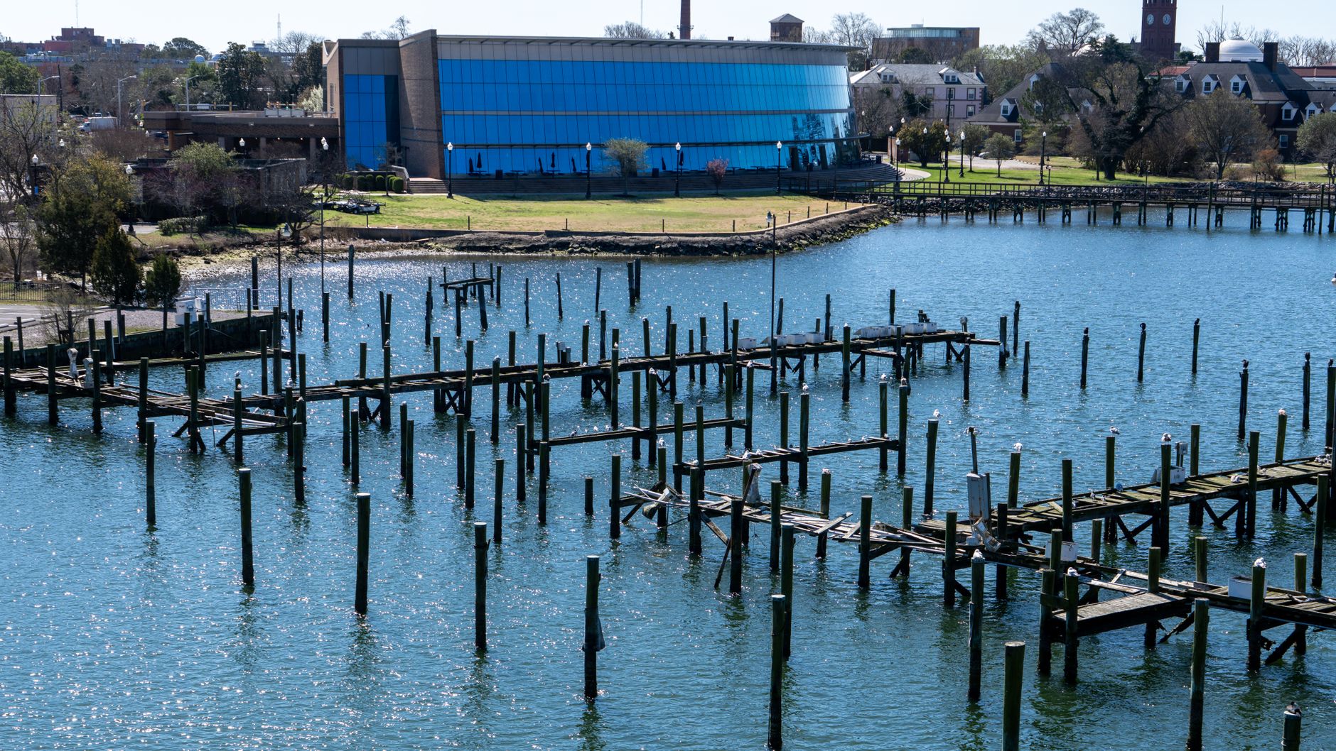 Aerial view of a waterfront and wooden pier in Hampton, Virginia with calm waters and cityscape in the background.