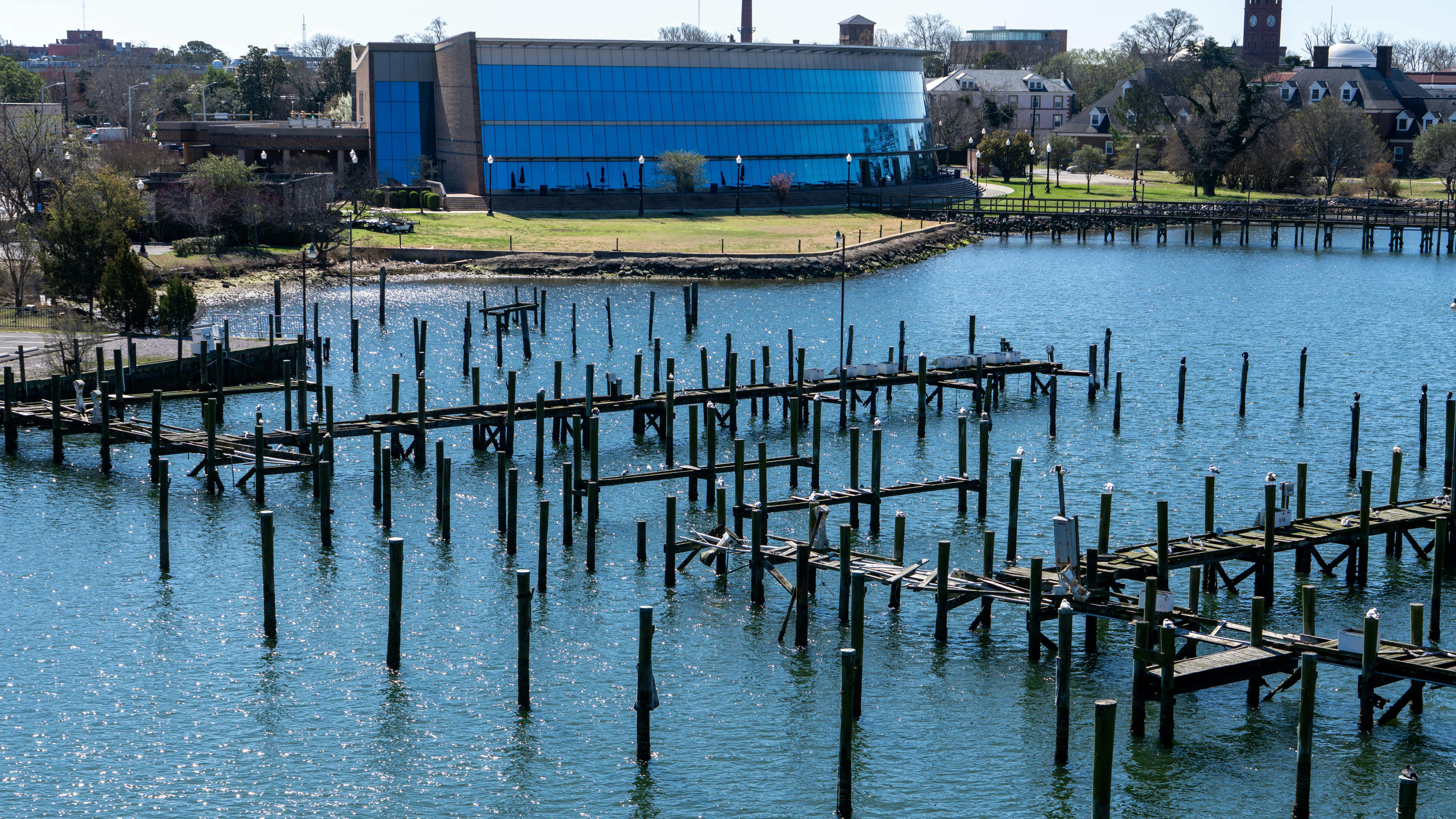 Kostnadsfria Flygfoto över en strandpromenad och en träpir i Hampton, Virginia med lugnt vatten och stadsbild i bakgrunden. Stock foto
