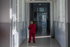 A nurse in red scrubs walks through a sunlit corridor in a hospital setting.