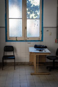 An empty hospital room with a table, chairs, and a frosted window casting light inside.