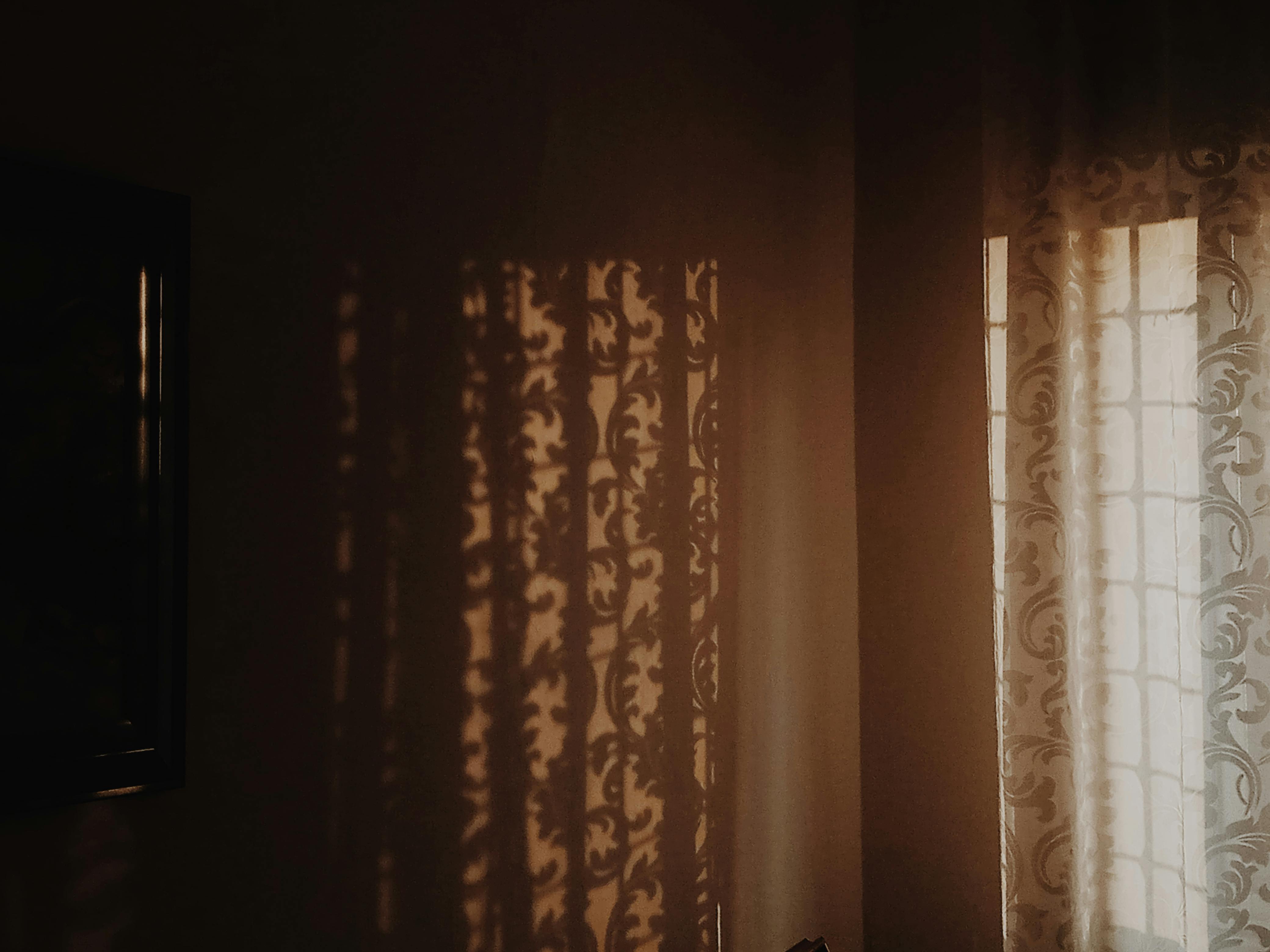 Безкоштовне Тепле сонячне світло відкидає складні тіні крізь візерунчасті штори в затишному приміщенні. стокове фото