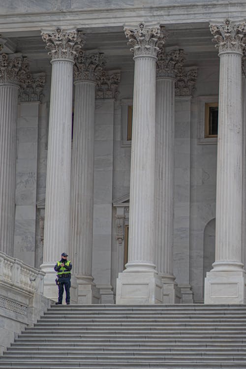 免費 一名警官站在建築物的白色混凝土柱子附近 圖庫相片
