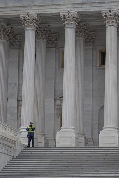 A Police Officer Standing Near White Concrete Pillars Of A Building