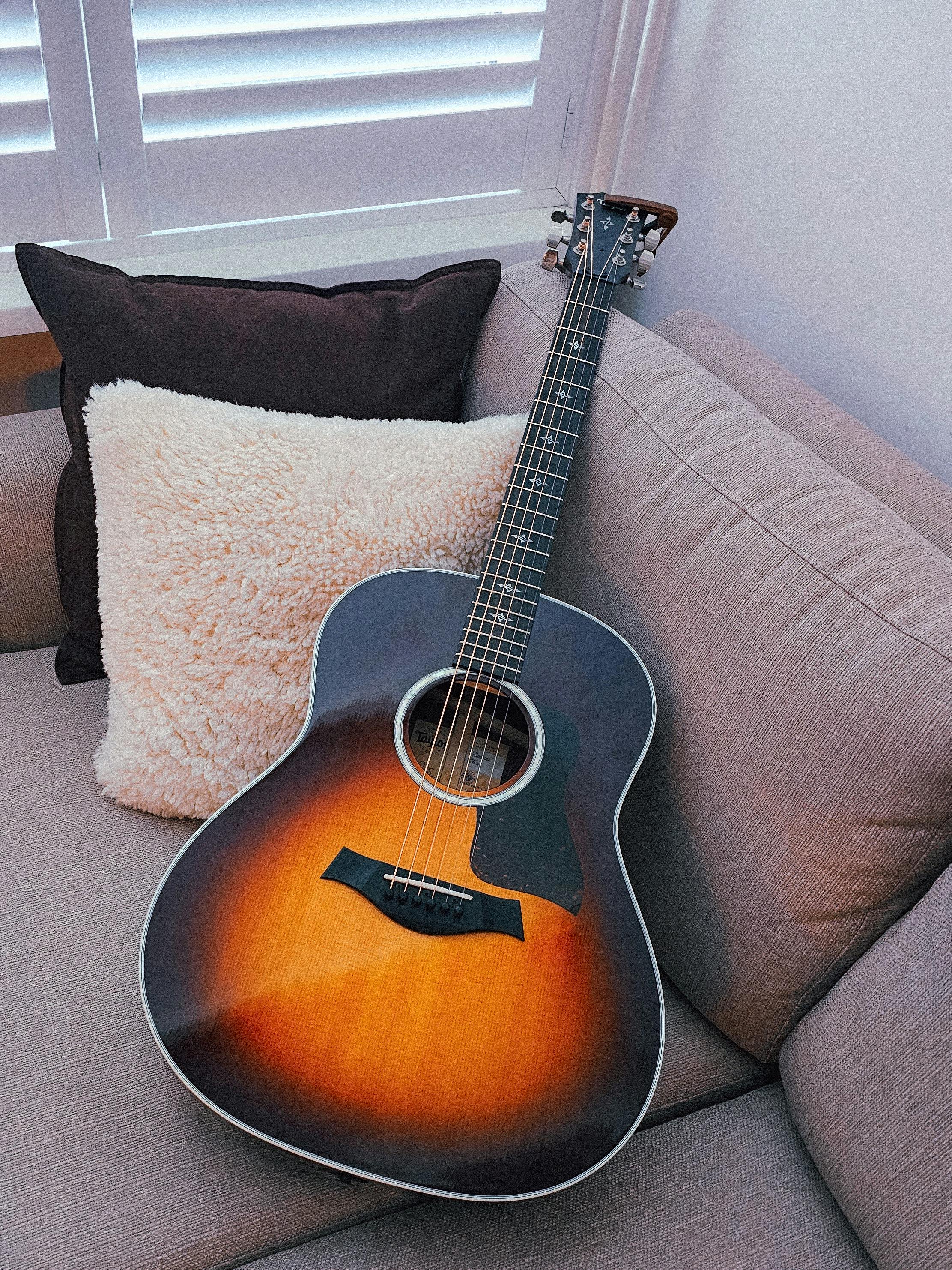 免費 一把旭日色原聲吉他靜靜地放在舒適的沙發上，柔軟的靠墊環繞四周，沐浴在柔和的自然光中。 圖庫相片