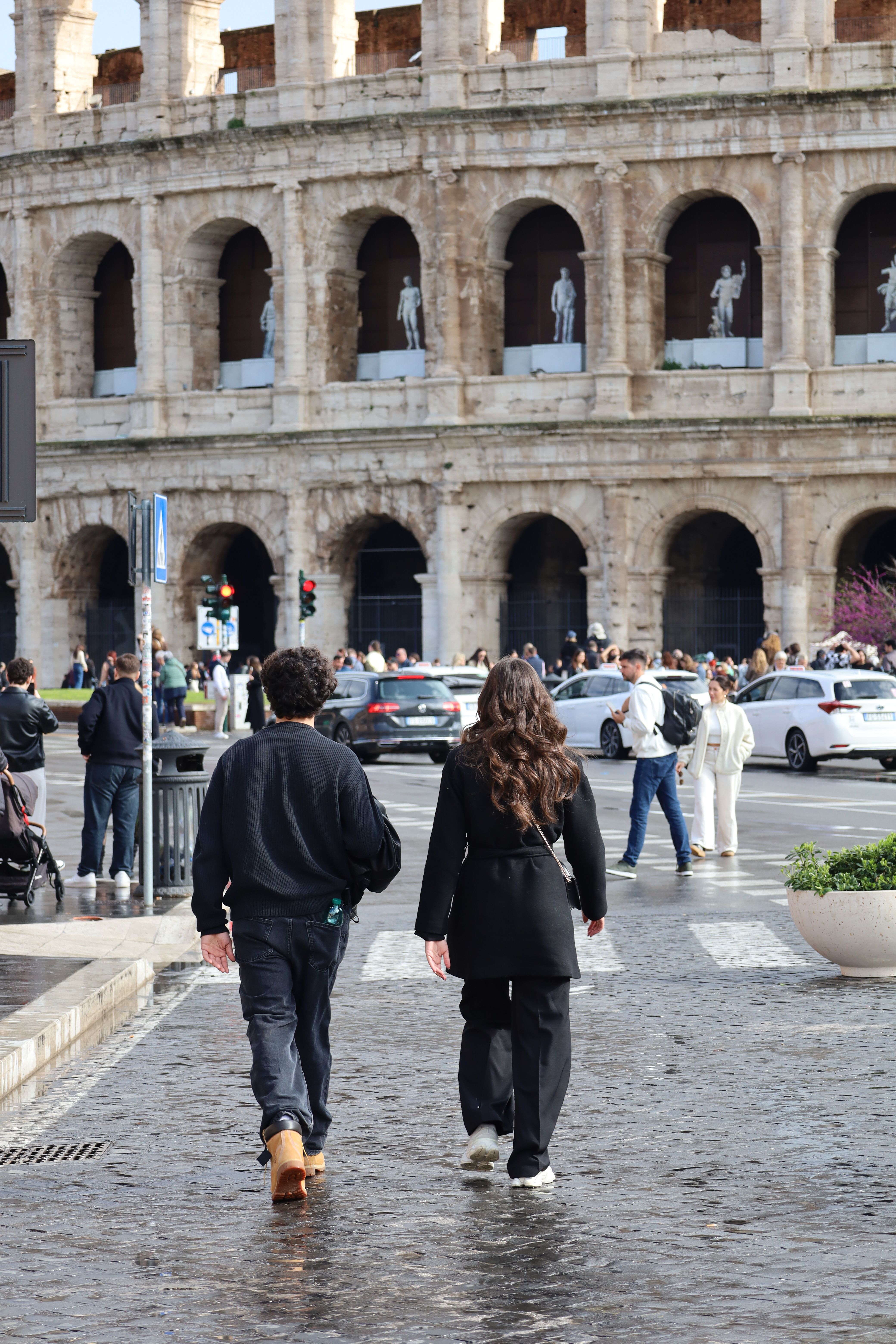 Two people walking by the iconic Colosseum in Rome, capturing the historic and bustling atmosphere.
