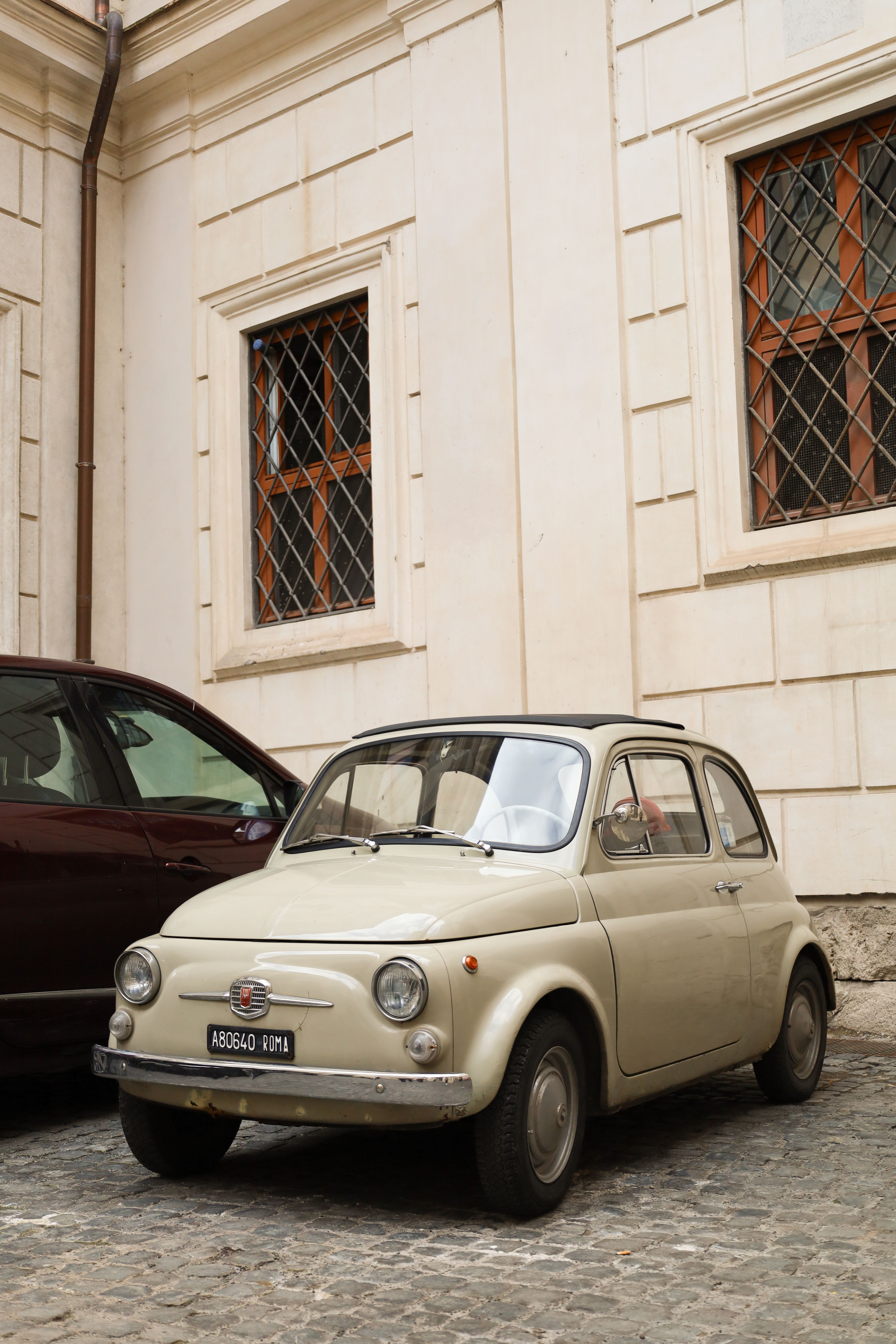 Classic Fiat 500 parked on a cobblestone street in Rome, showcasing historical architecture and Italian charm.