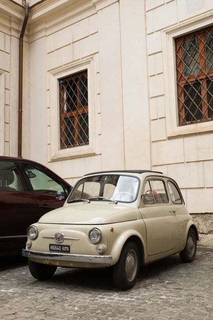 Classic Fiat 500 parked on a cobblestone street in Rome, showcasing historical architecture and Italian charm.