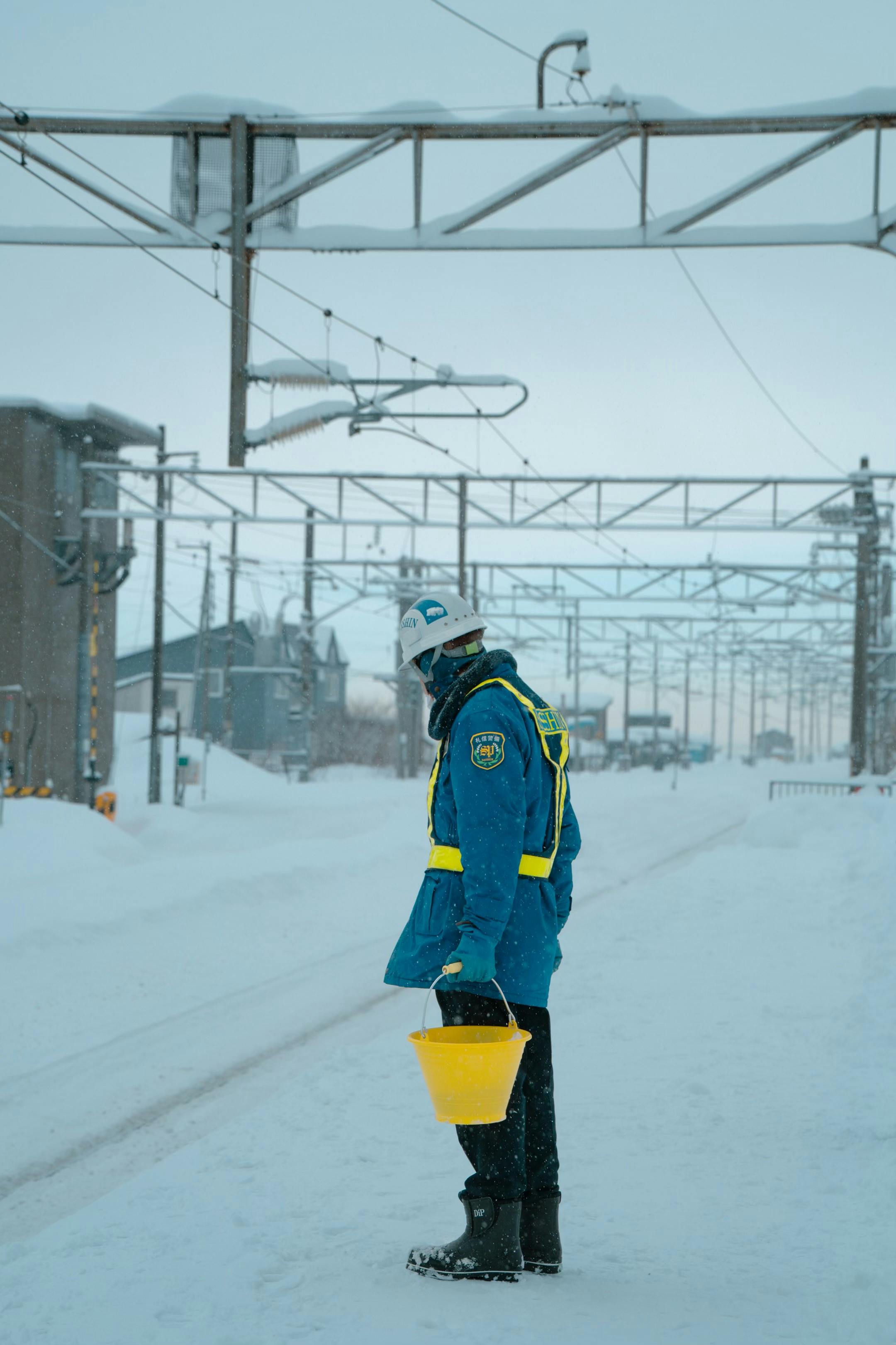 Kostnadsfria En arbetare står på en snöig gata i Sapporo, Japan, under vintern och håller i en gul hink. Stock foto