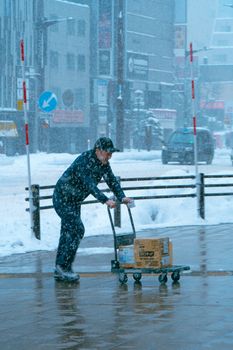 A man pushing a cart through heavy snow in Sapporo, capturing urban winter life.