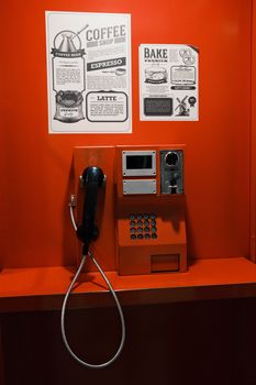 Retro red payphone booth indoors with coffee shop posters on the wall.