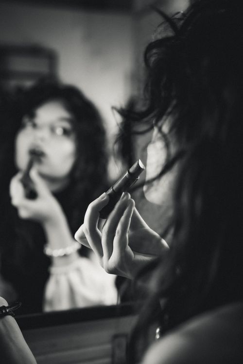 Free Monochrome image of a woman applying dark lipstick in front of a mirror, capturing a moment of personal reflection. Stock Photo