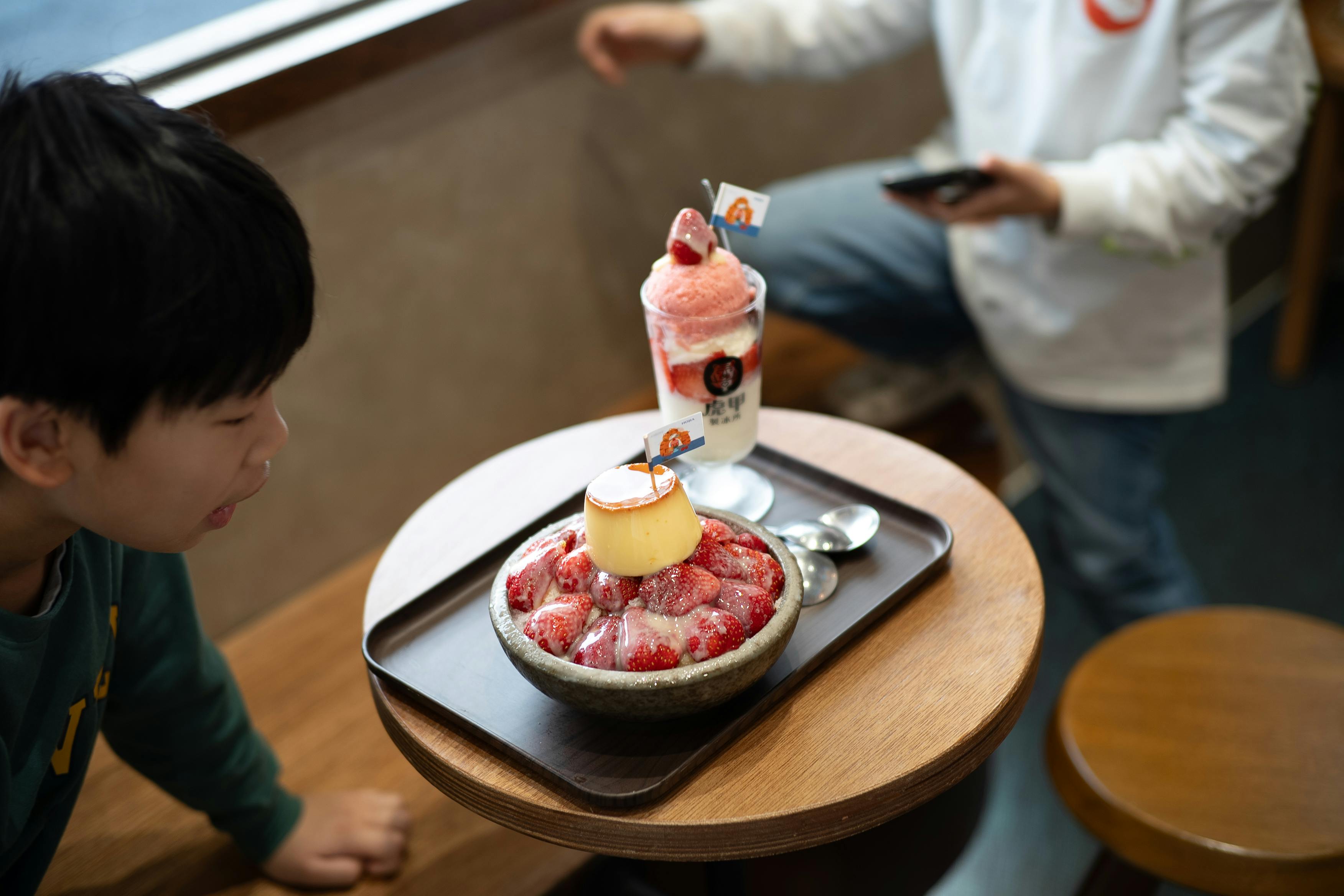 ingyenes Közeli kép egy epres desszertről, miközben a gyerekek finomságokat fogyasztanak bent. Hangulatos és kellemes légkör. Stockfotó